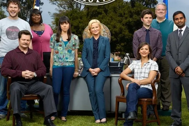 The cast of Parks and Recreation posing outdoors, including Leslie Knope, Ron Swanson, and Andy Dwyer. A great TV show.