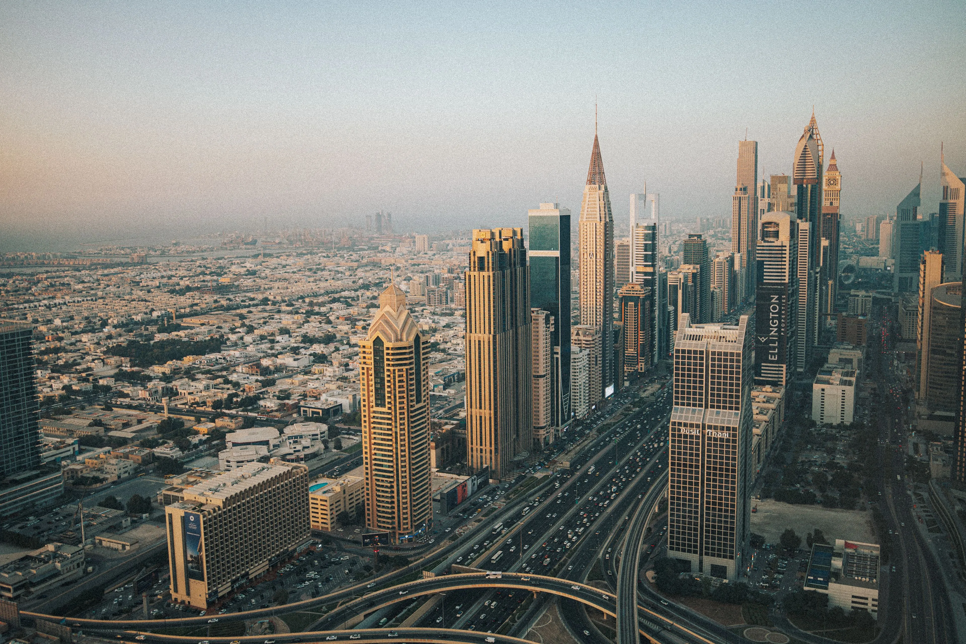 Aerial view of the stunning UAE cityscape at sunset, with numerous skyscrapers and busy highways leading into the city.
