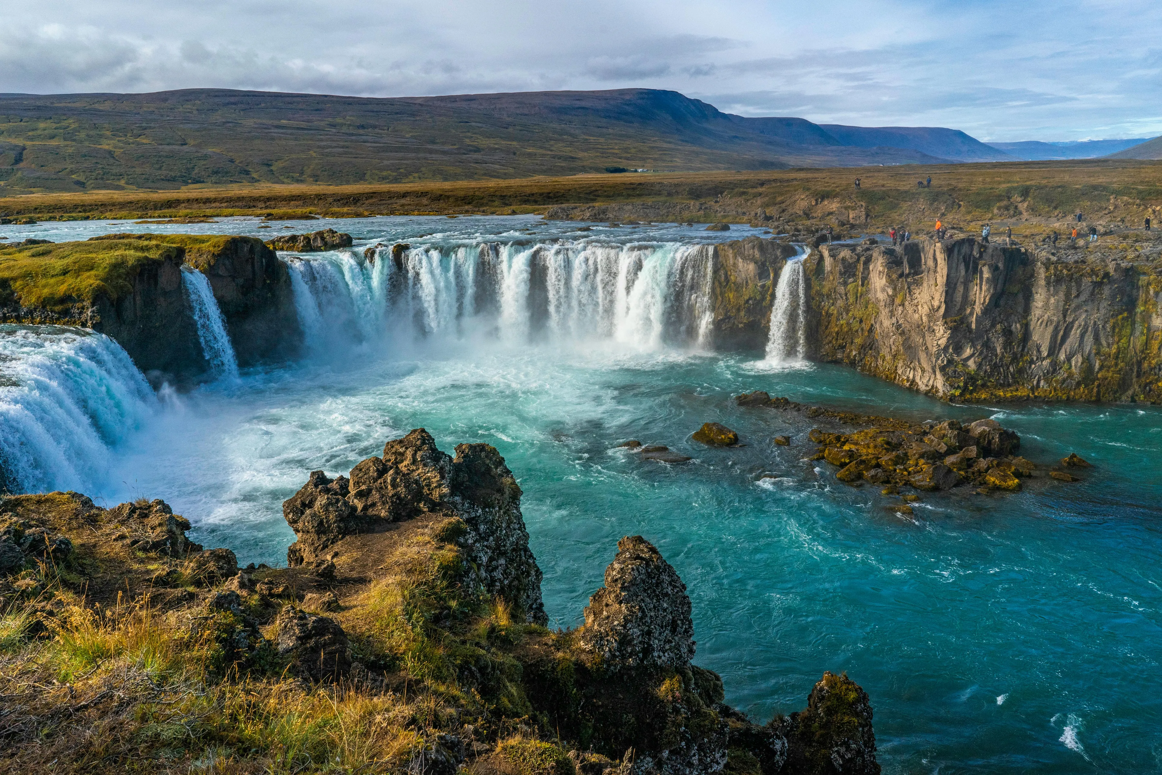 Dramatic wide shot of Godafoss waterfall in Iceland, a beautiful holiday destination, with turquoise water and green banks.