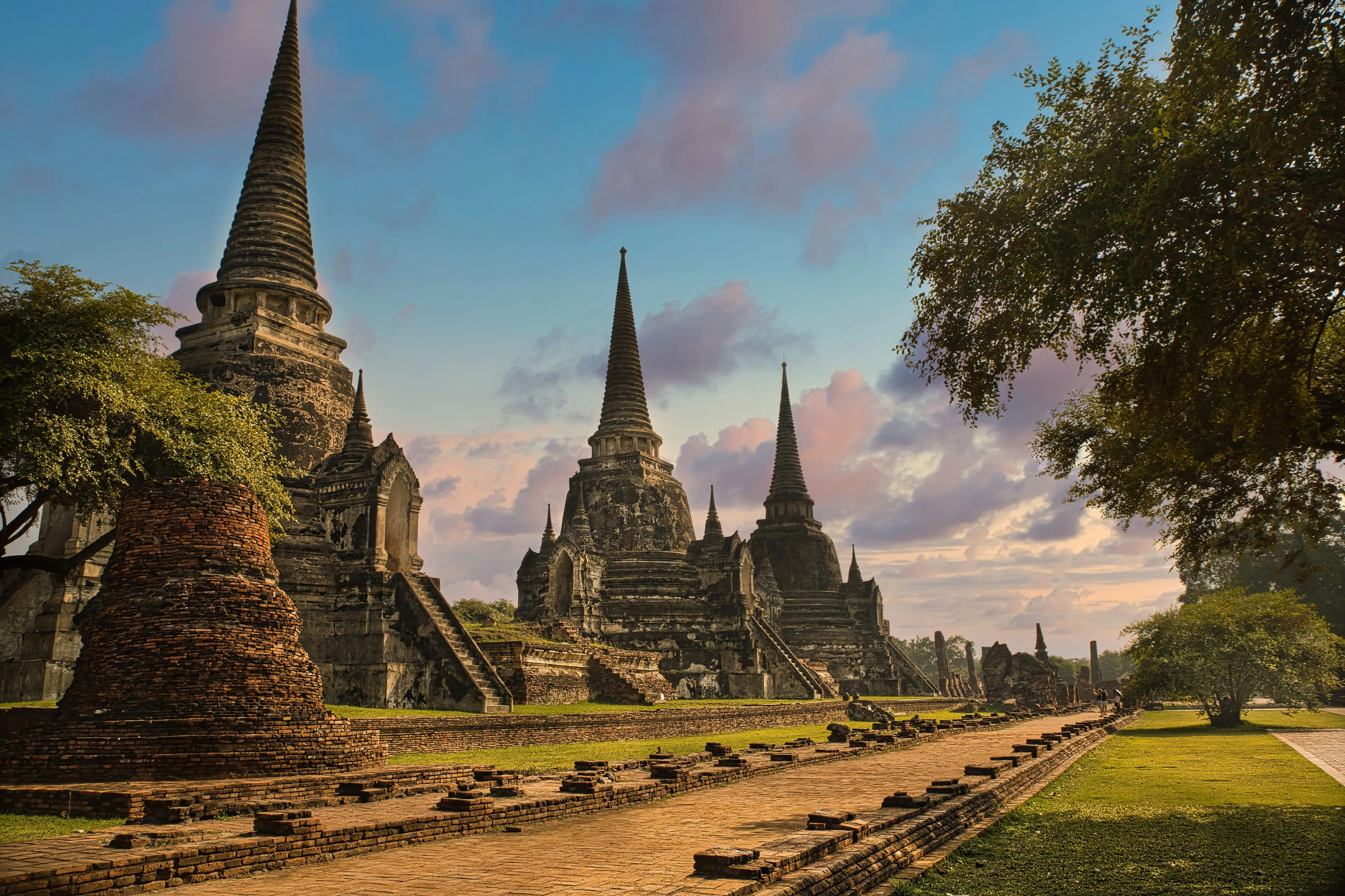 Ancient temples with towering spires at sunset, a beautiful holiday destination in Thailand, surrounded by green trees.