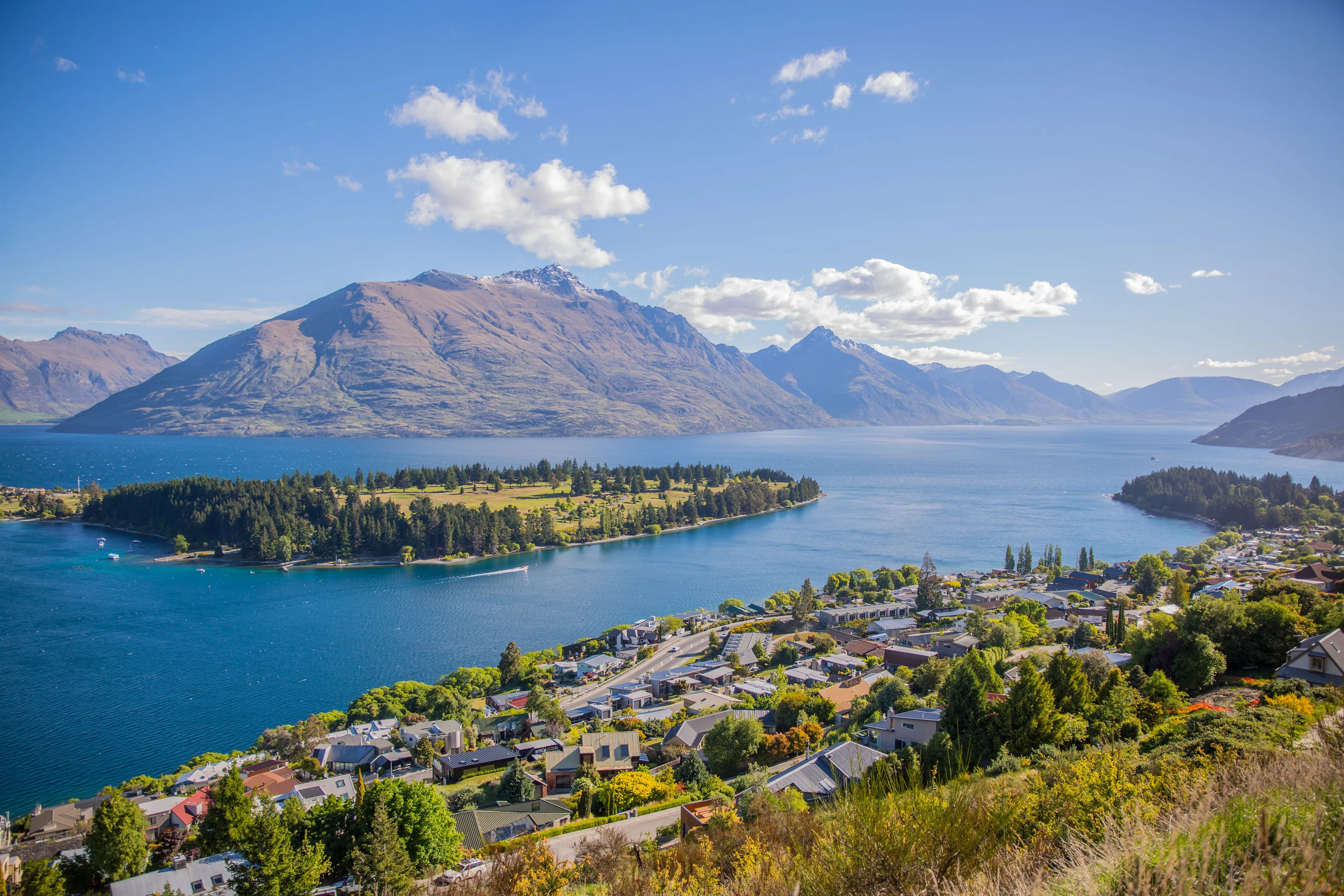 Panoramic view of Lake Wakatipu, Queenstown, New Zealand, with a town nestled by the water and majestic mountains.