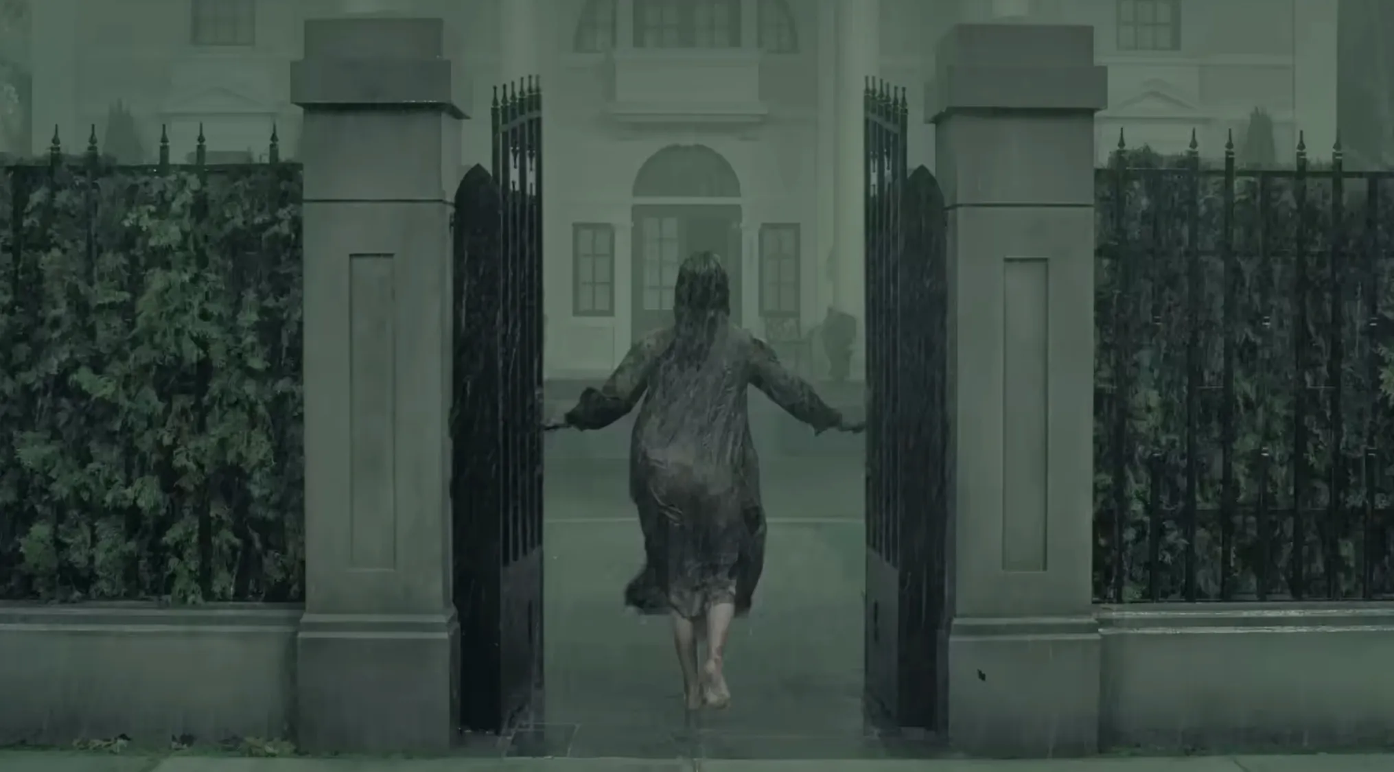 A barefoot person in a soaked dress walks through large gates in the rain, evoking The Fall of the House of Usher.