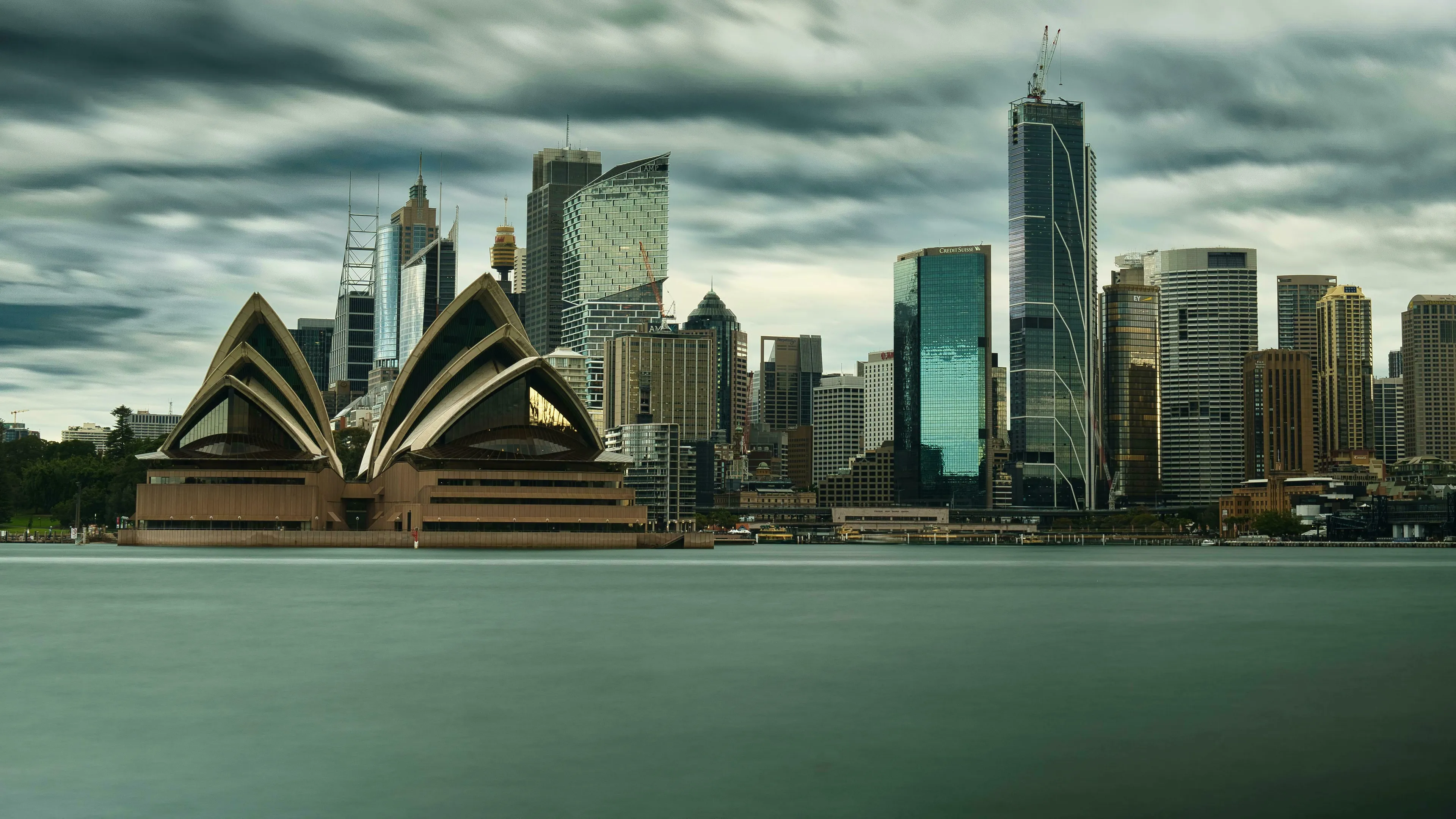 A scenic view of the Sydney Opera House and the Australian skyline, reflecting on the water under a cloudy sky. Australian currency.
