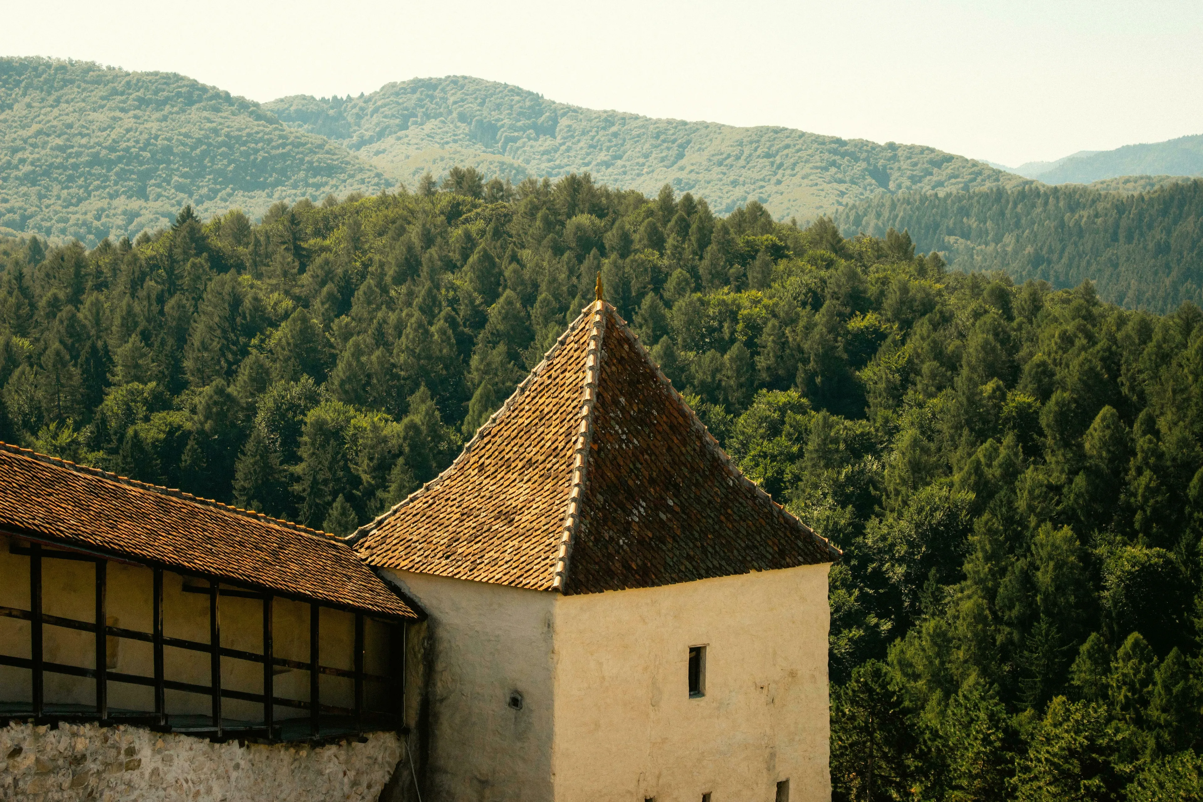 A fortified tower in Transylvania, Romania with a brown tiled roof, against a backdrop of lush green forests and hills.