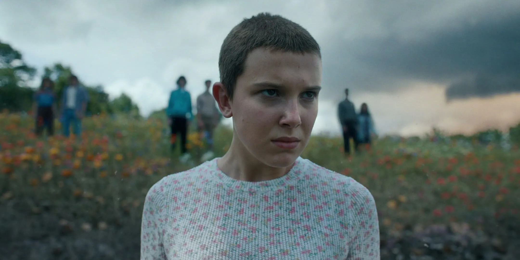 Eleven from the TV series Stranger Things, with short hair and a floral sweater, standing in a field. Pub Quiz.