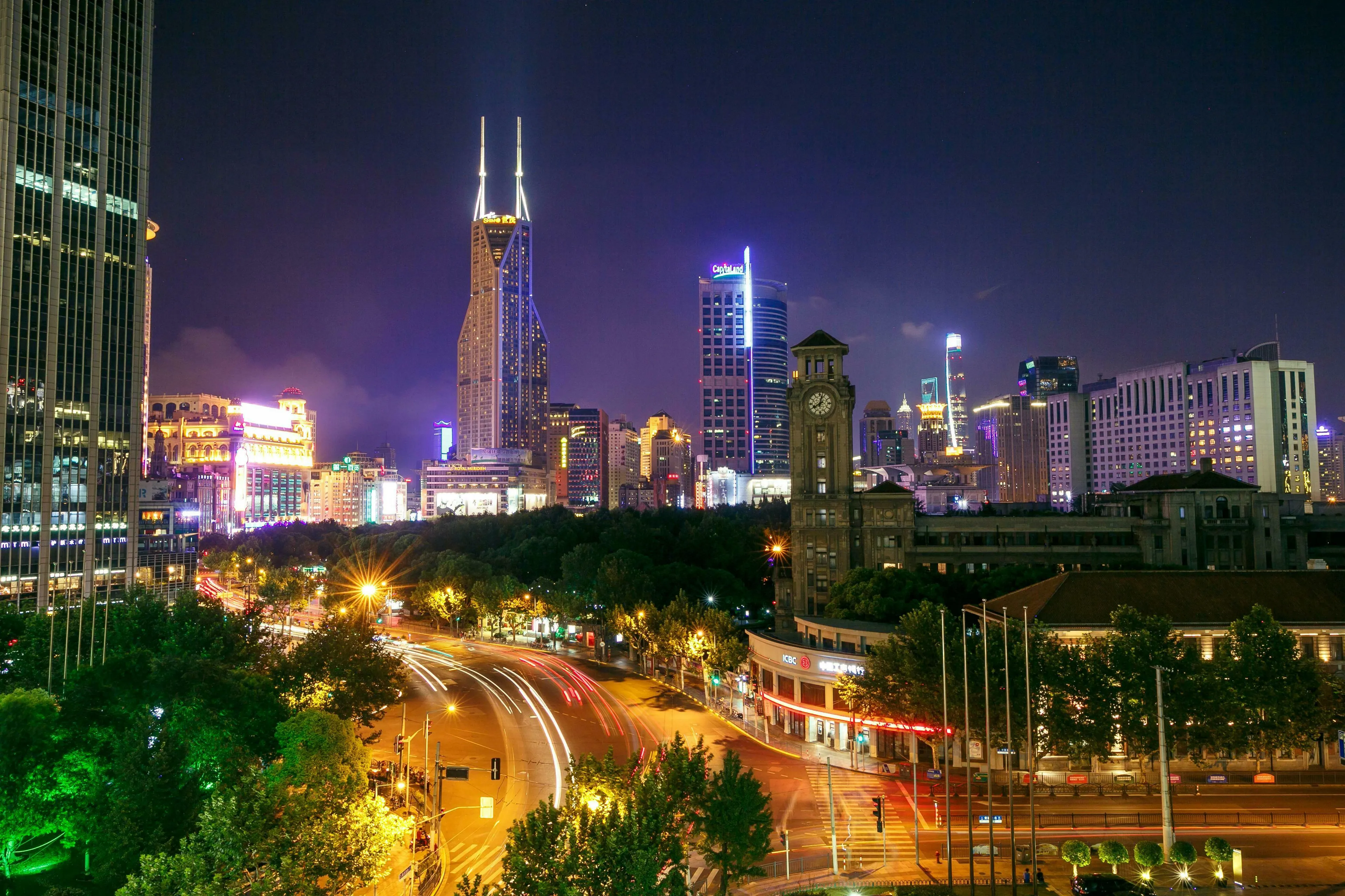 Night view of Shanghai city skyline with illuminated skyscrapers, a clock tower, and cars on a busy road.