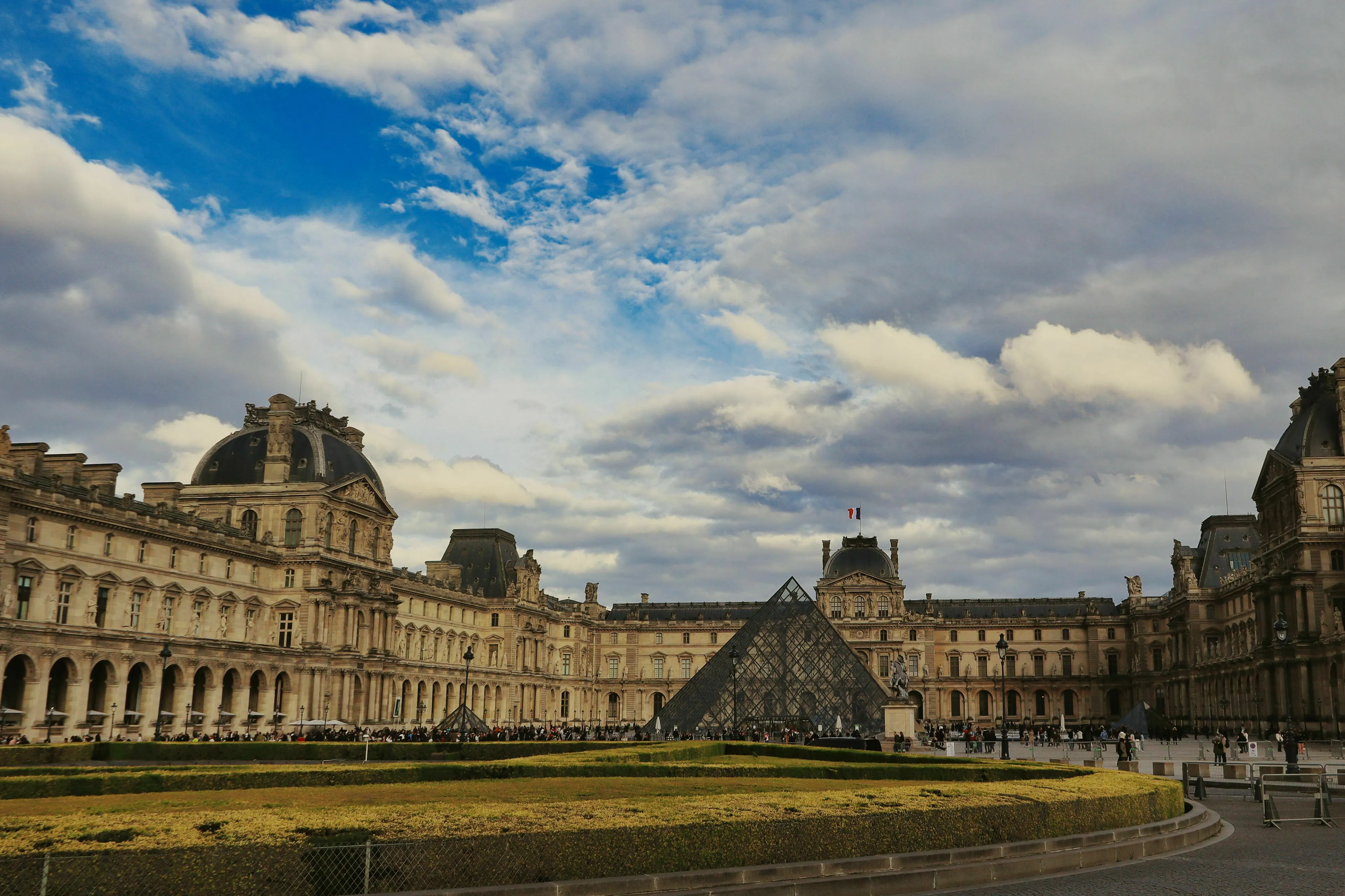 The Louvre Museum in Paris, France, with its iconic pyramid under a cloudy sky, showcasing its grand architecture.
