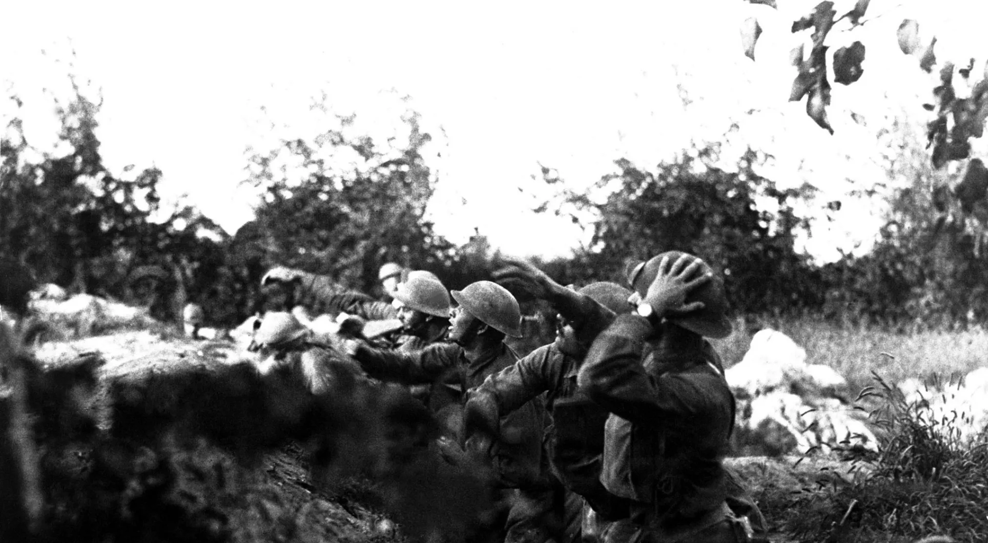 Black and white photo of soldiers in helmets, possibly USA troops, ducking in a trench during World War I.