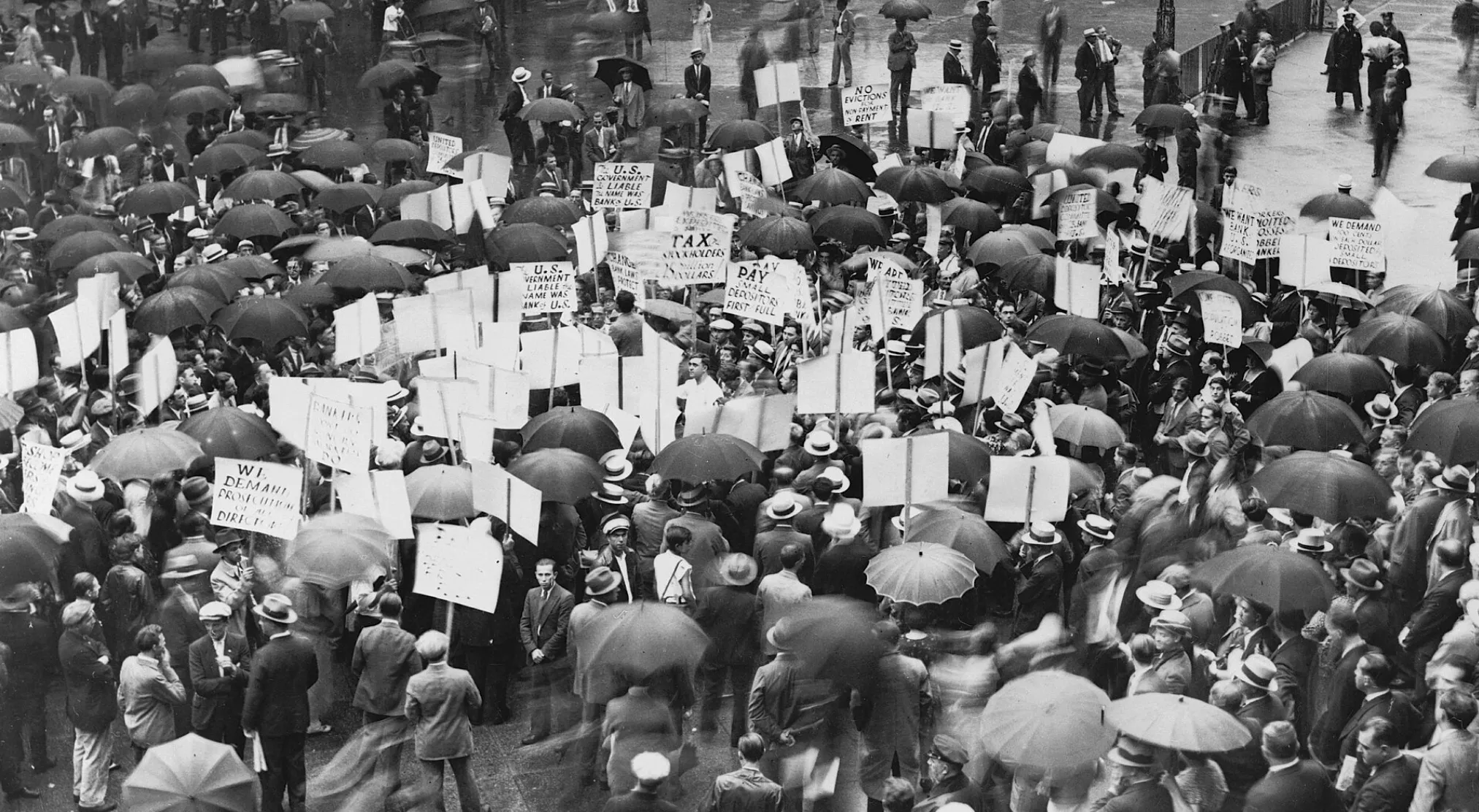 Black and white photo of people with umbrellas and protest signs, reflecting a USA during the Great Depression.