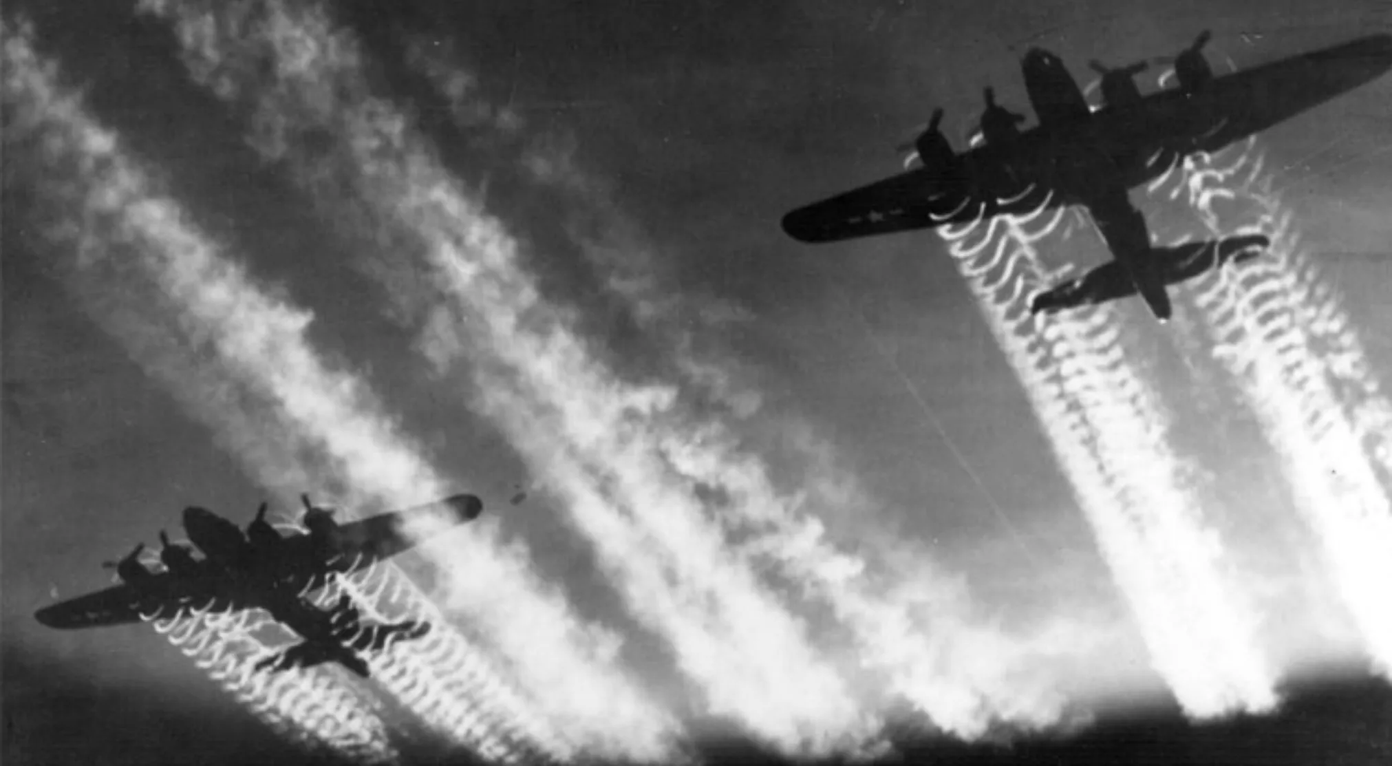 Two B-17 bombers in flight, silhouetted against a cloudy sky, with prominent contrails. World War II history.