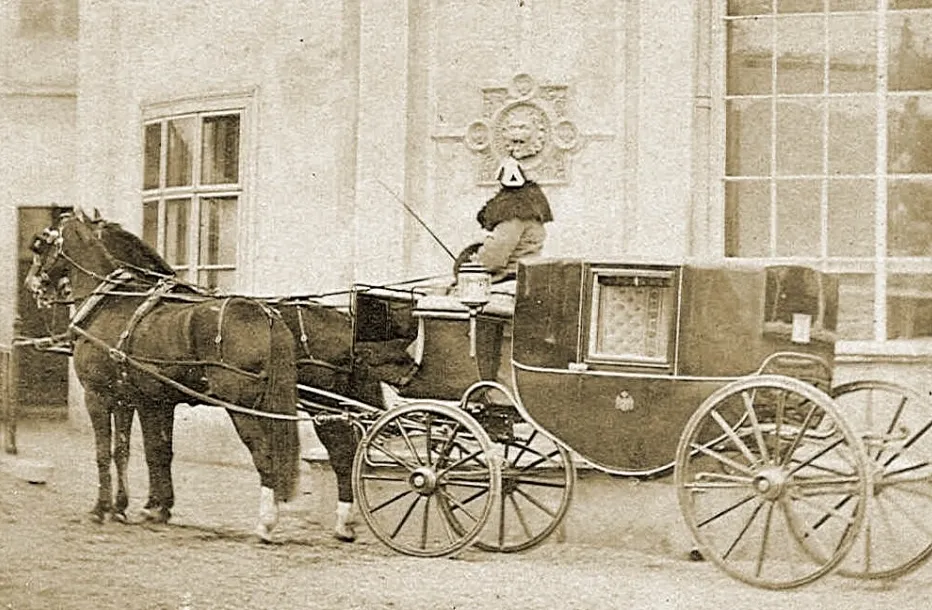 Sepia photo of a horse-drawn carriage with a driver, parked near a building. Carriages were key to Industrial Revolution travel and trade.
