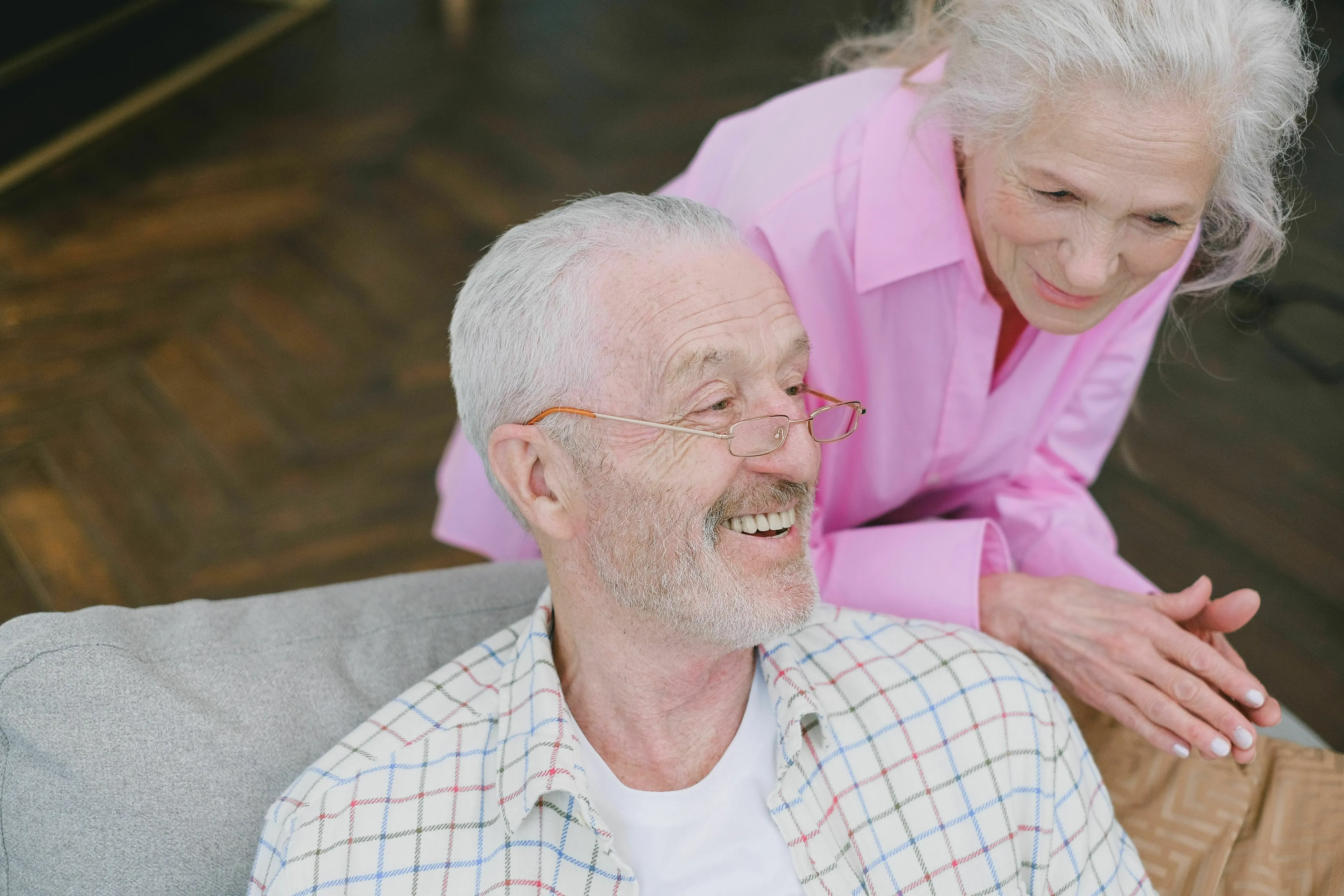 A happy senior couple, the man smiling while the woman gently touches his shoulder. Reflects on growing older.