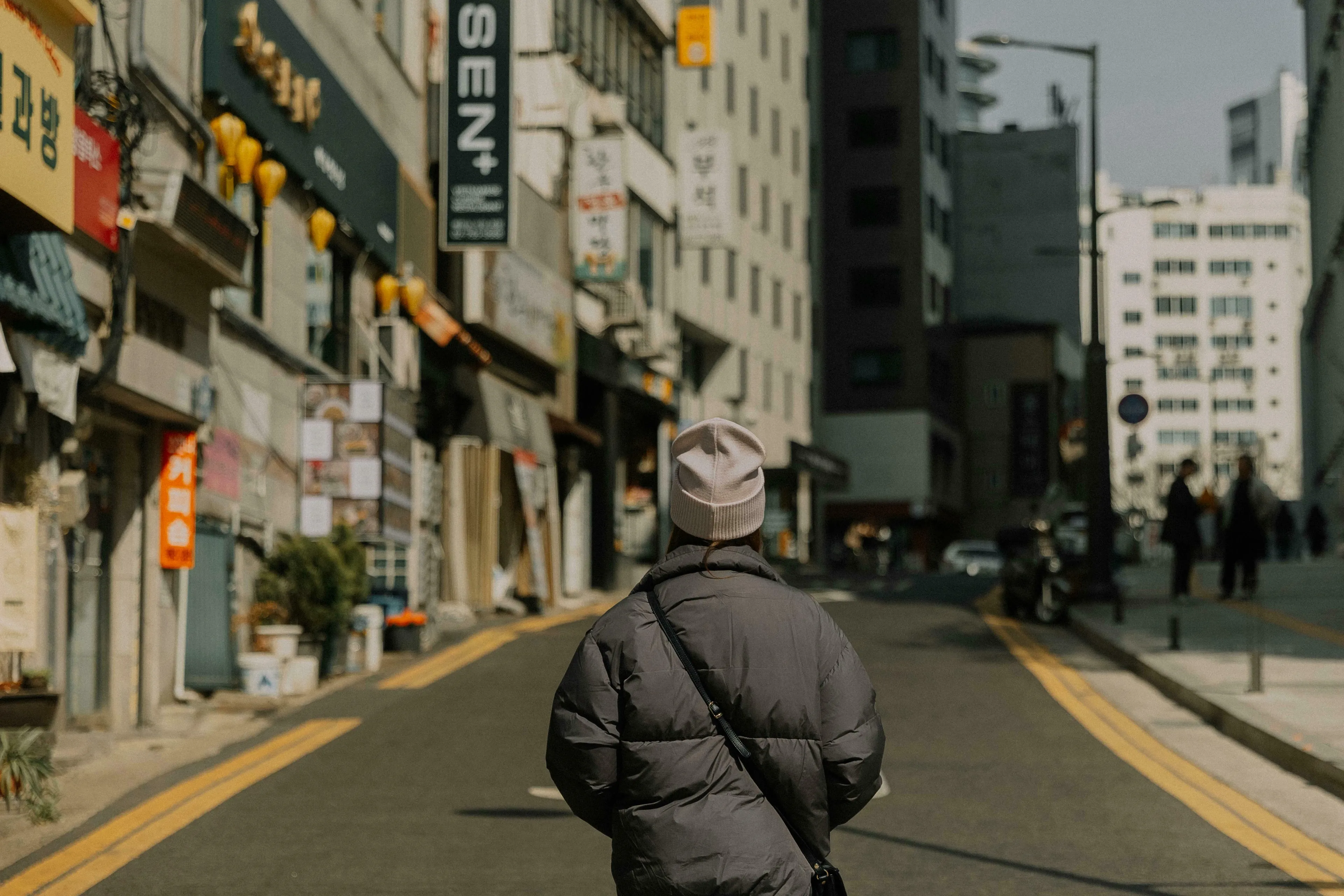 A person in a puffer jacket and beanie walks down a city street, reflecting the season and true nature.