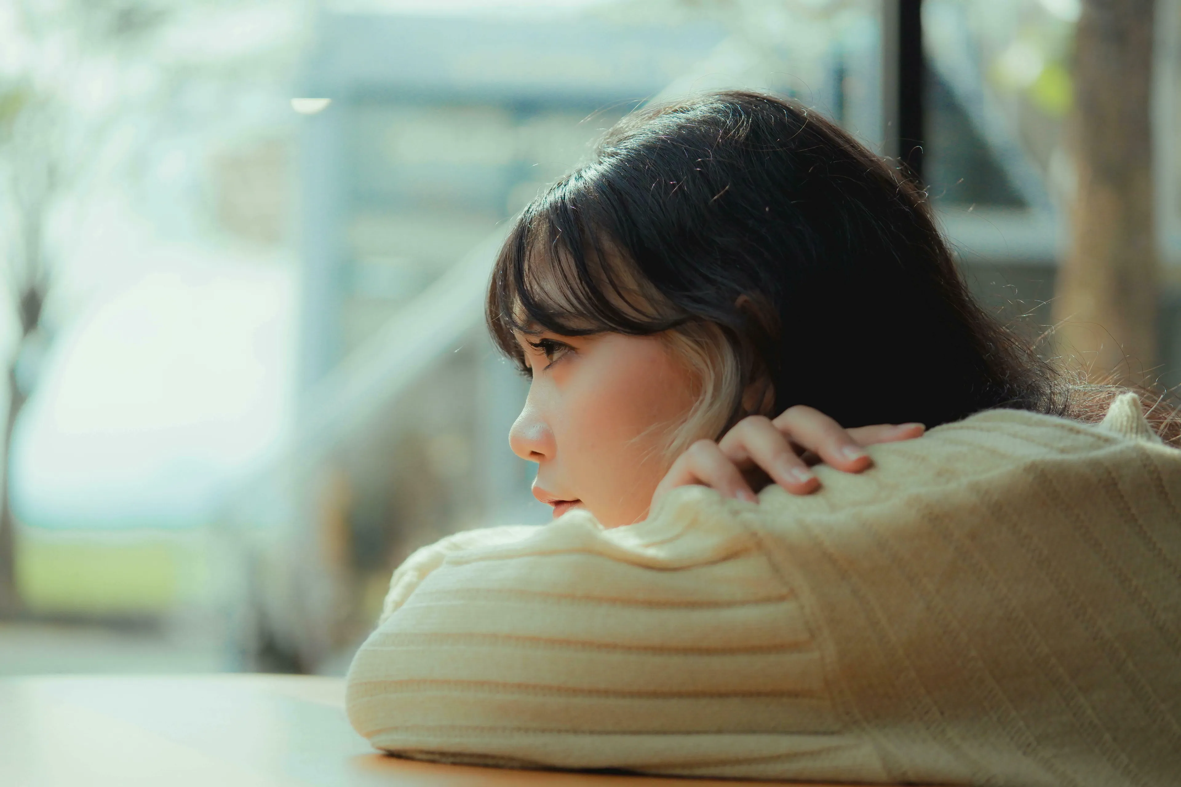 Young woman with dark hair and a blonde streak, looking out a window, contemplating a big life decision or her true nature.