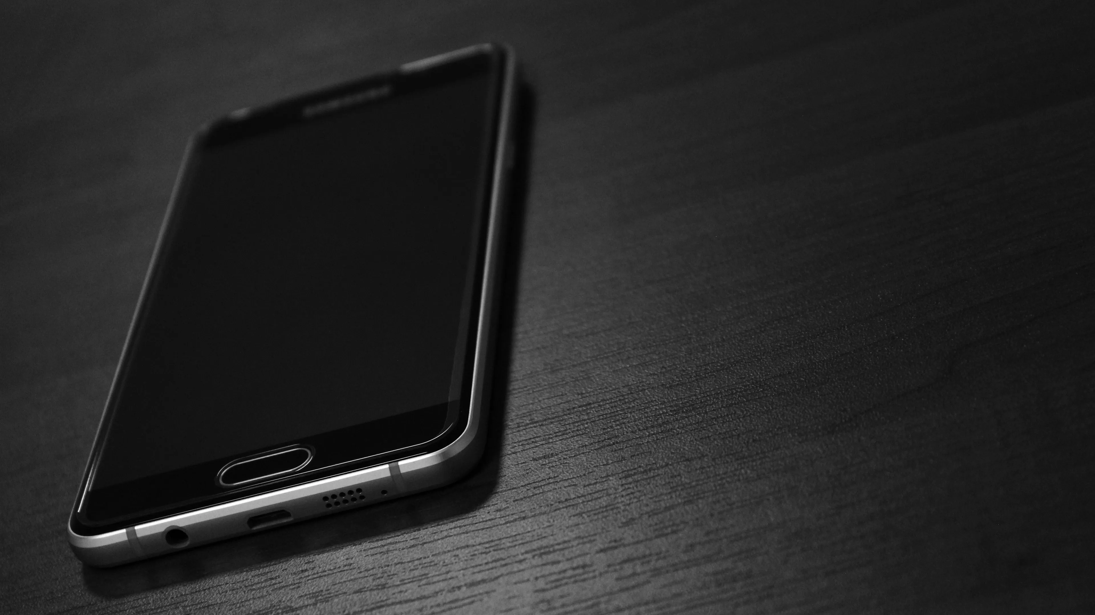 A phone, screen off, on a dark table, evoking feelings about Your True Nature and a dead phone.