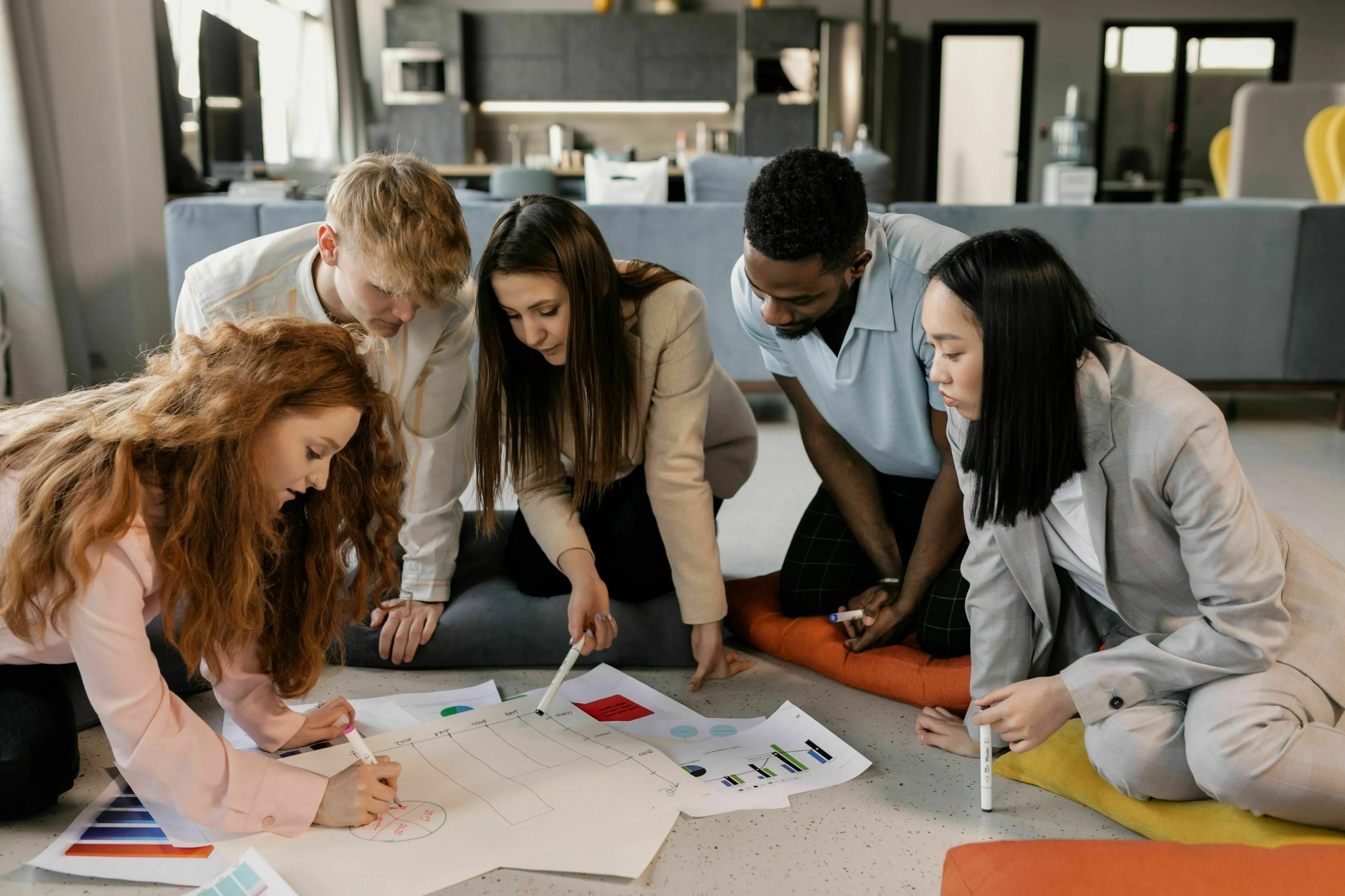 Diverse group collaborating on a group project, sketching ideas and reviewing charts on the floor. Which season reflects your true nature?