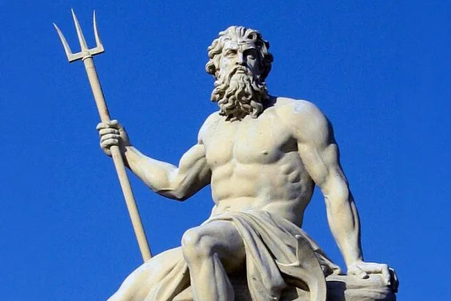 A detailed statue of Poseidon, the Greek god of the sea, holding his trident against a clear blue sky.