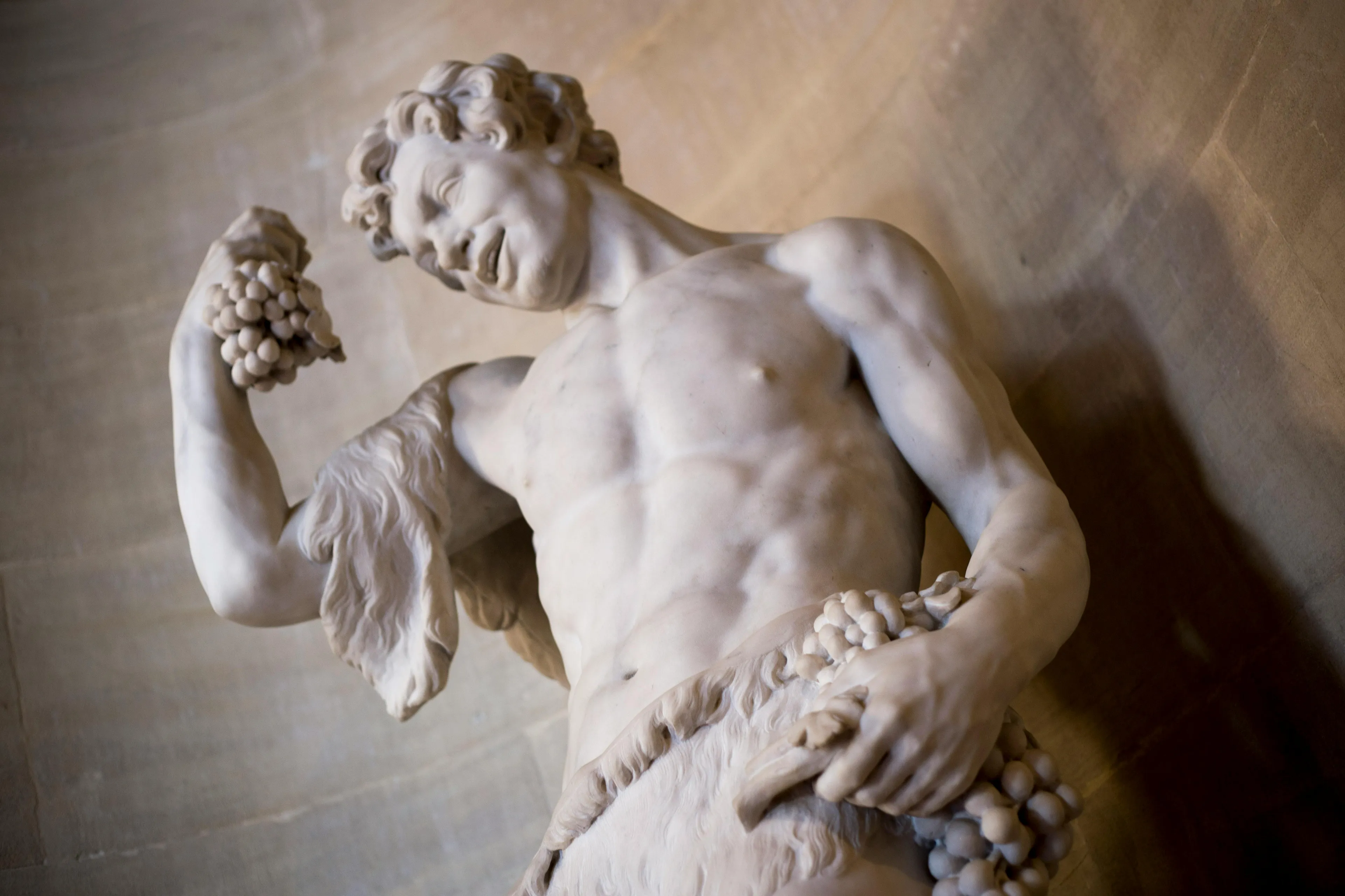 A marble statue of a muscular Greek god, Dionysus, holding bunches of grapes, depicting joy and revelry.