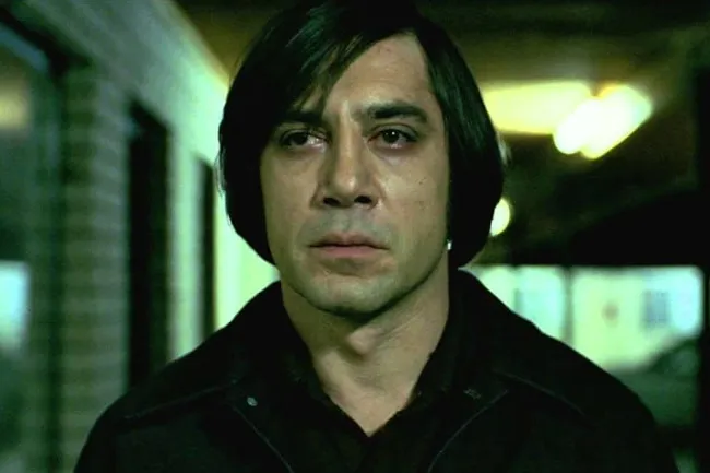 Javier Bardem as Anton Chigurh in No Country for Old Men, staring intently with his iconic haircut.
