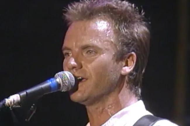 Sweaty Sting, lead singer of The Police, singing Every Breath You Take into a microphone on stage.