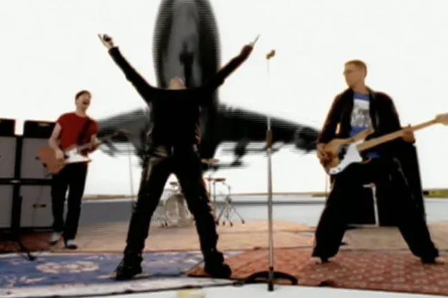 U2 performs Beautiful Day, Bono with arms raised in front of a jet, The Edge & Adam Clayton on guitars.