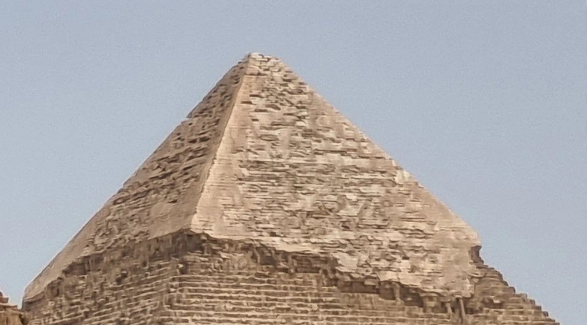 Zoomed-in photo of the Great Pyramid of Giza. Guess the landmark, a huge stone structure against a light sky.