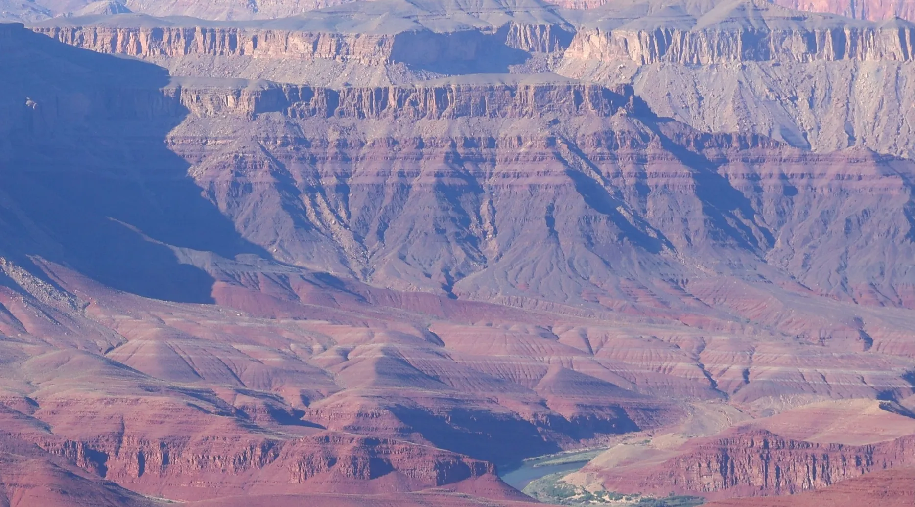 Zoomed-in photo of the Grand Canyon, revealing layers of reddish-brown rock formations and a glimpse of the Colorado River below. Guess the landmark.