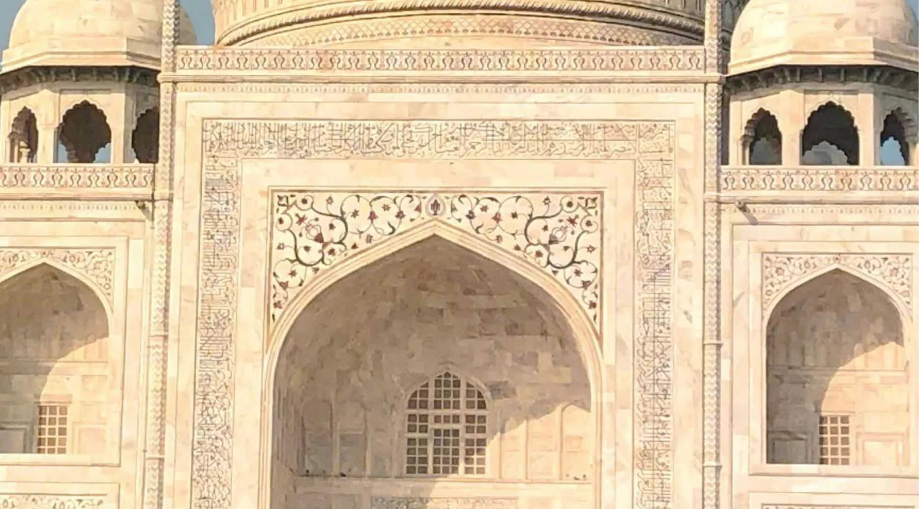 Guess the landmark from the zoomed-in photo. Intricate marble carvings and arches, characteristic of the Taj Mahal.