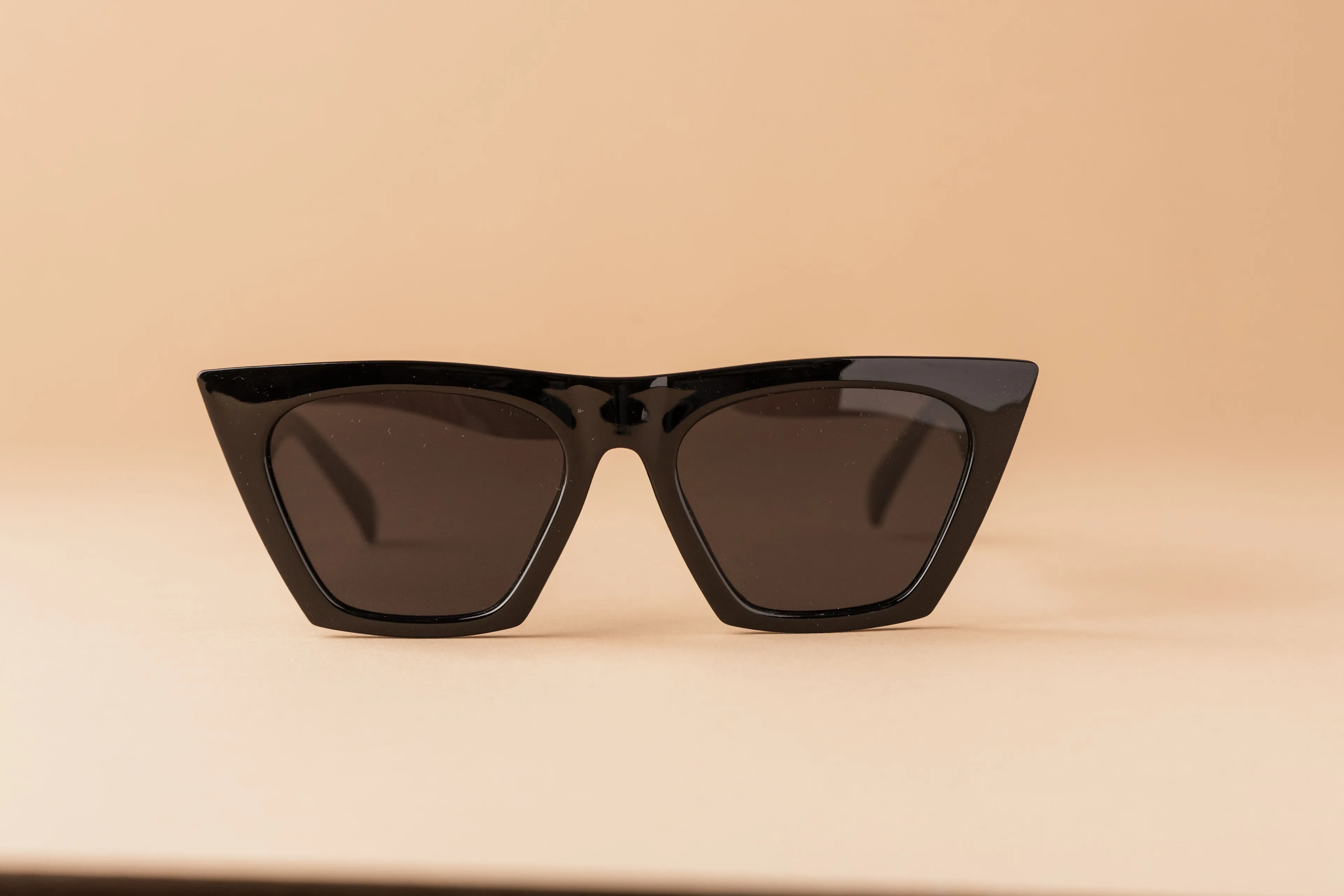 Stylish black cat-eye sunglasses with dark lenses on a neutral background, a classic fashion trend.