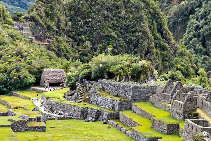 Guess the landmark from the zoomed-in image: ancient stone ruins with terraced fields and thatched roofs, surrounded by lush green mountains.