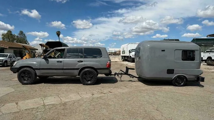 Grey SUV towing a matching vintage camper trailer parked outside, highlighting old products still reliable today.