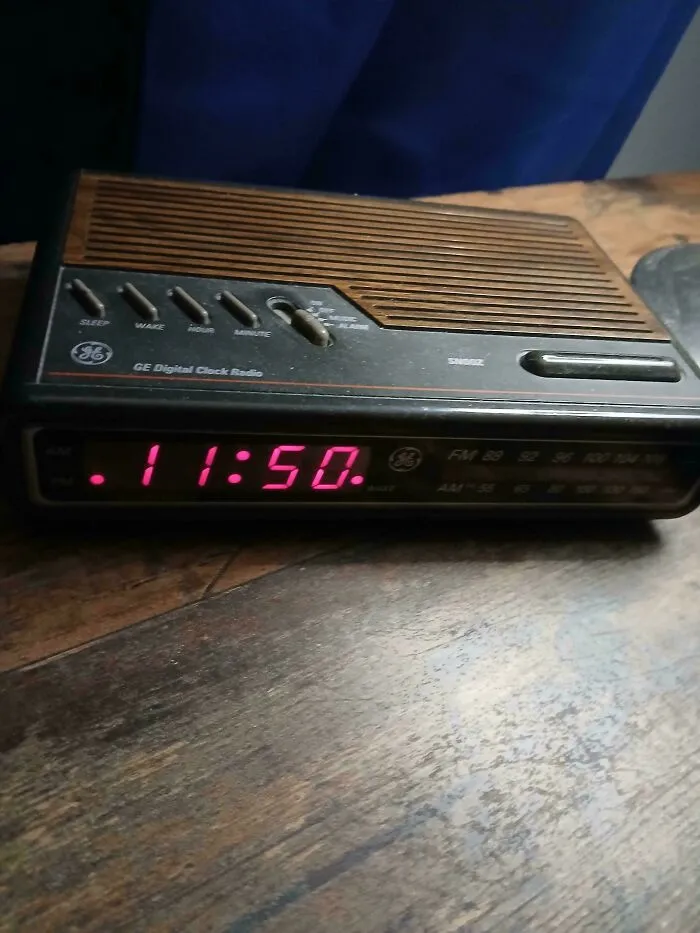A vintage GE digital clock radio with a red LED display sitting on a wooden desk, showcasing old products built to last