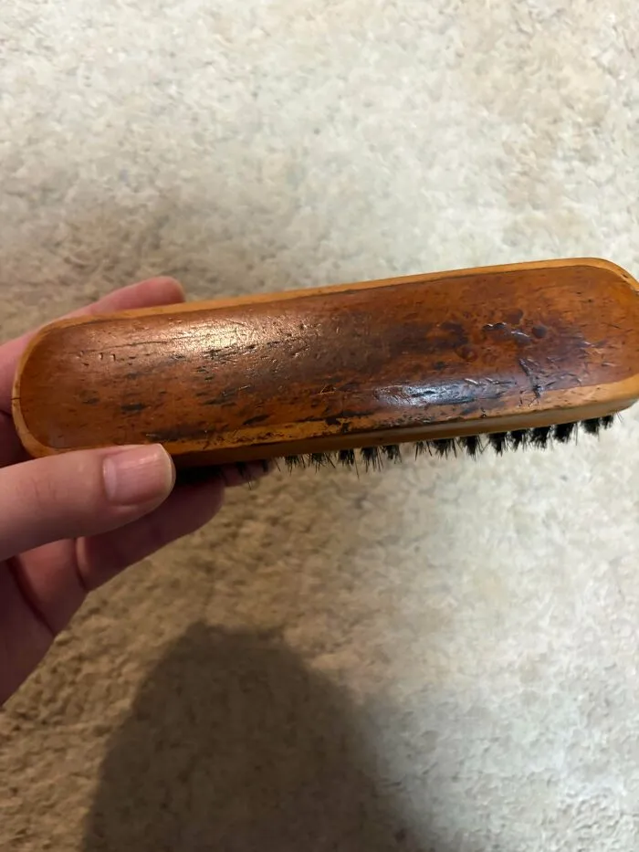 A hand holding a vintage wooden brush, exemplifying old products that remain functional after daily use.