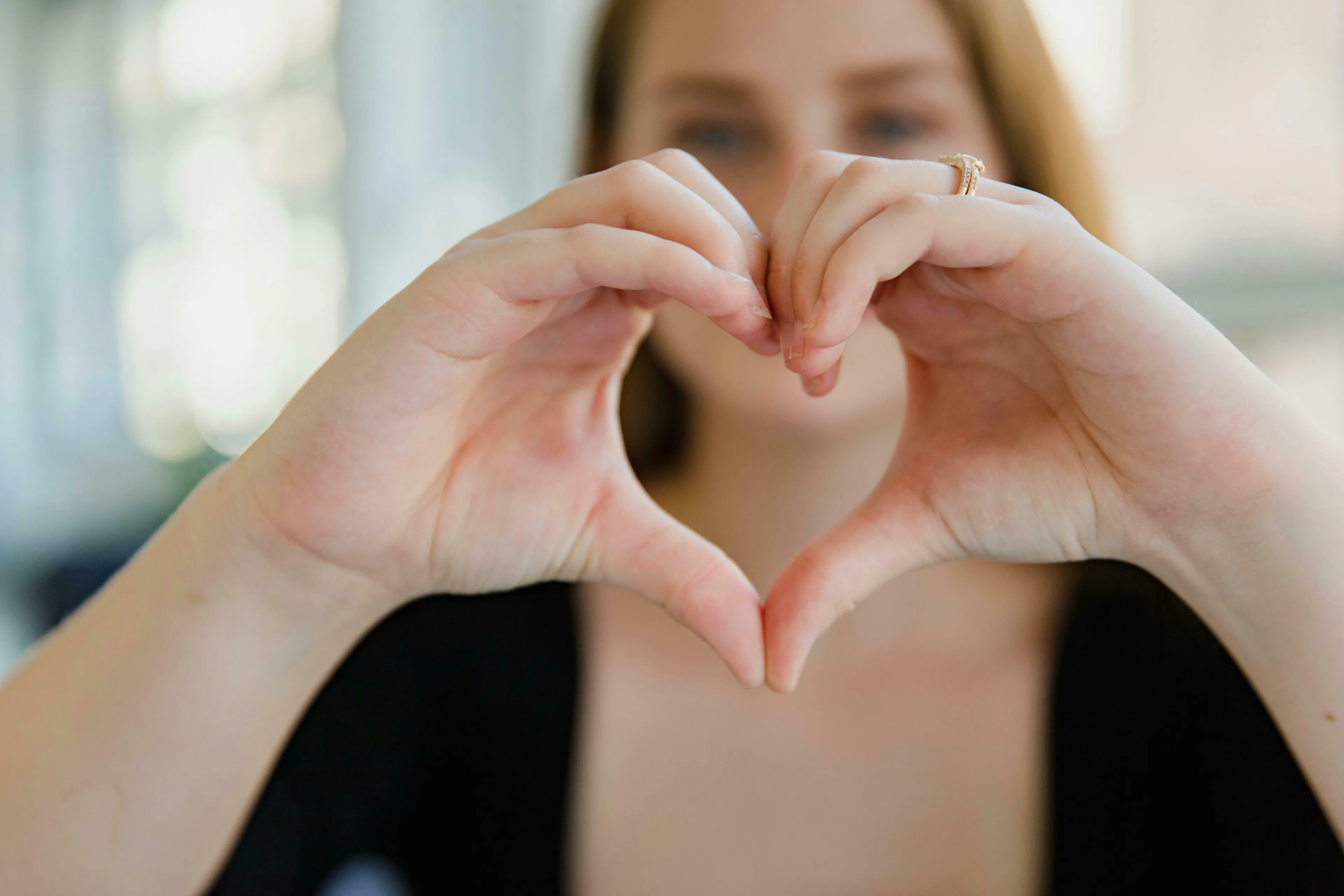 Woman with light brown hair making a heart shape with her hands. A human heart is crucial for general knowledge.