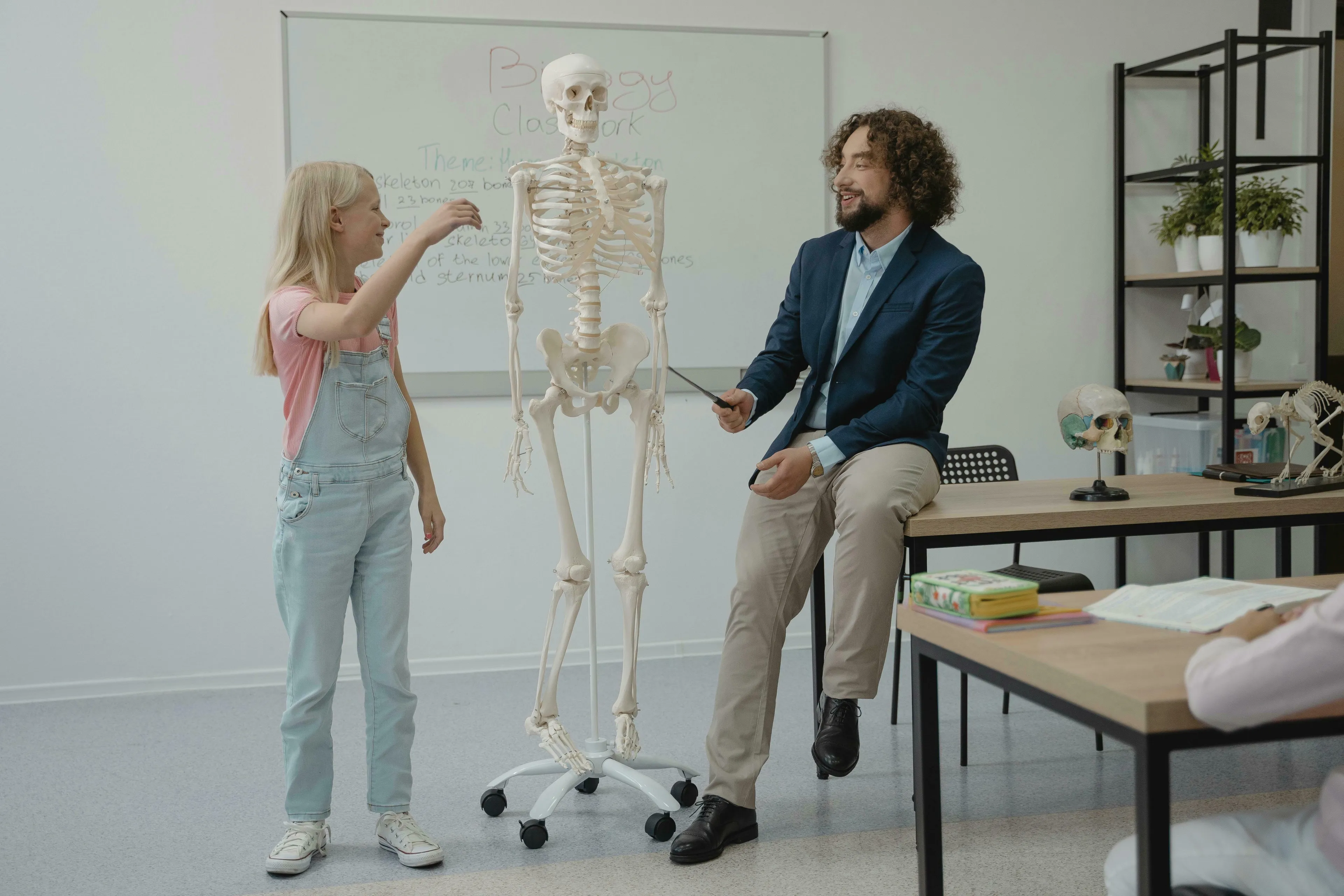 A teacher and student in a biology class examining a human skeleton model. Discusses adult human bones vs. baby bones.