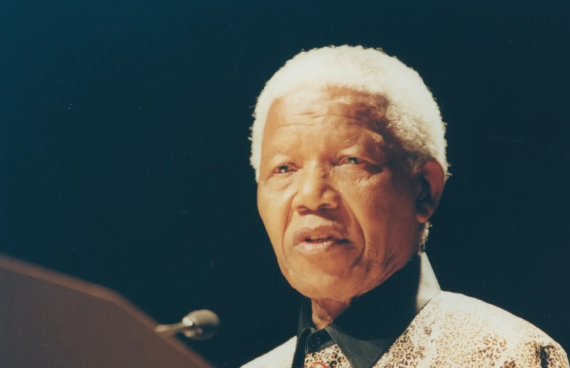 Nelson Mandela, with white hair, speaking at a podium. General Knowledge Quiz: Did Nelson Mandela become president of South Africa before or after prison?