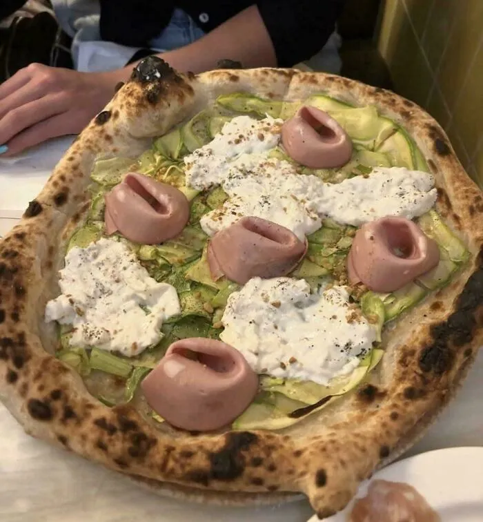 A pizza topped with zucchini, white cheese, and rolled ham slices showing questionable food combos.
