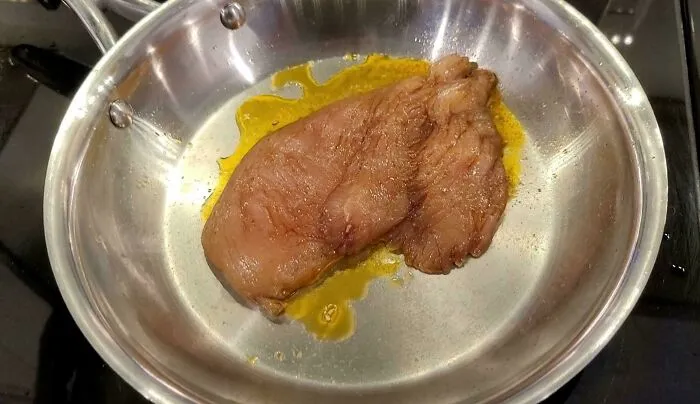 Raw chicken breast cooking in a pan with liquid, representing questionable food combos.