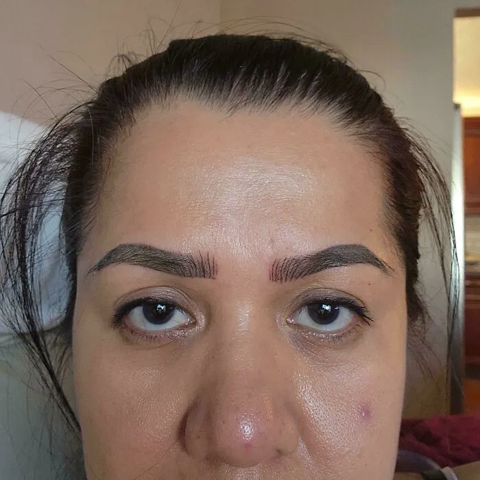 A woman looking significantly worse after a beauty salon eyebrow treatment, showing uneven and harshly drawn brows.