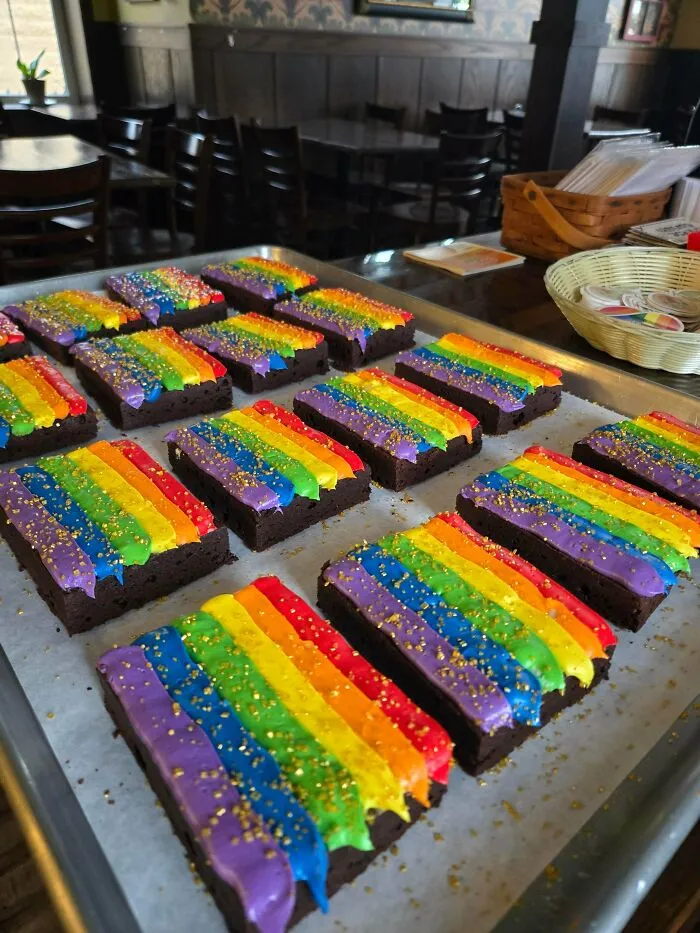 Delicious treats from a skilled baker: a tray of brownies with colorful rainbow frosting, sprinkled with gold dust.