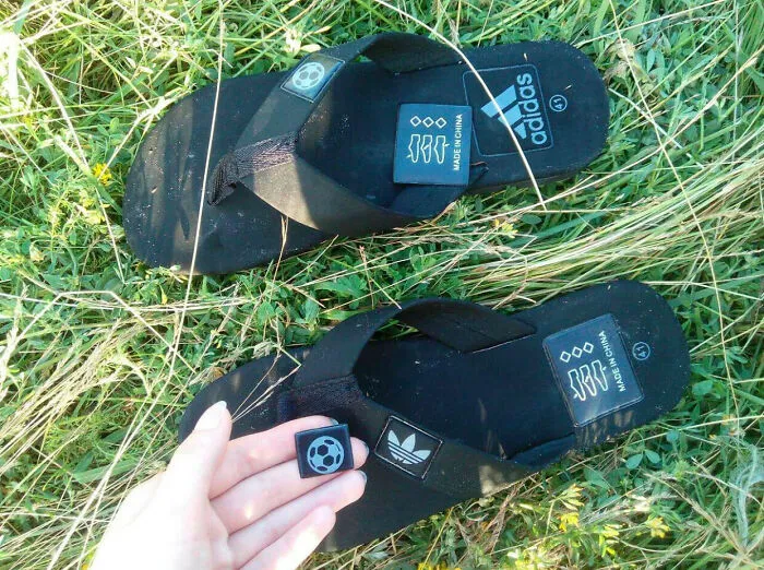 A pair of black sandals with adidas branding and a soccer ball logo, displaying bad clothing designs on grass.