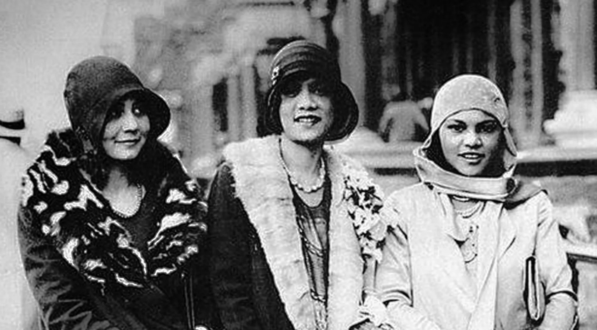 Black and white photo of three stylish women in cloche hats and fur stoles, embodying the Harlem Renaissance era.