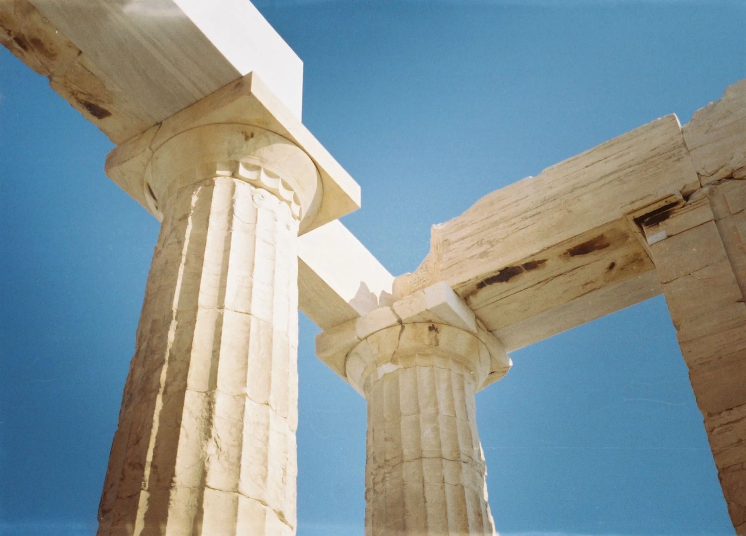 Looking up at ancient Greek philosopher temple ruins against a bright blue sky, showcasing detailed stone columns.