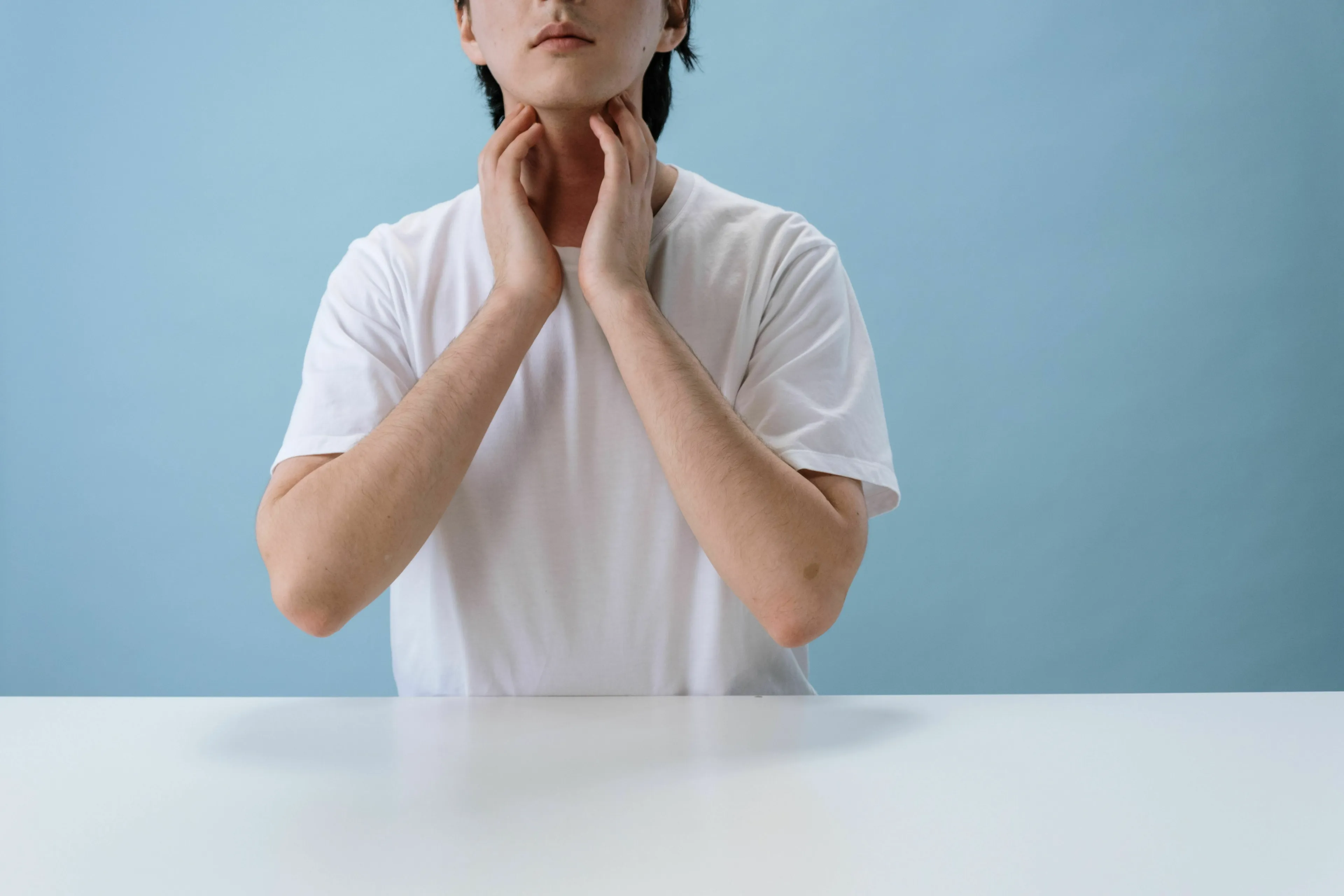 A person in a white shirt touches their neck, indicating the thyroid gland area. Science Human Biology Trivia.
