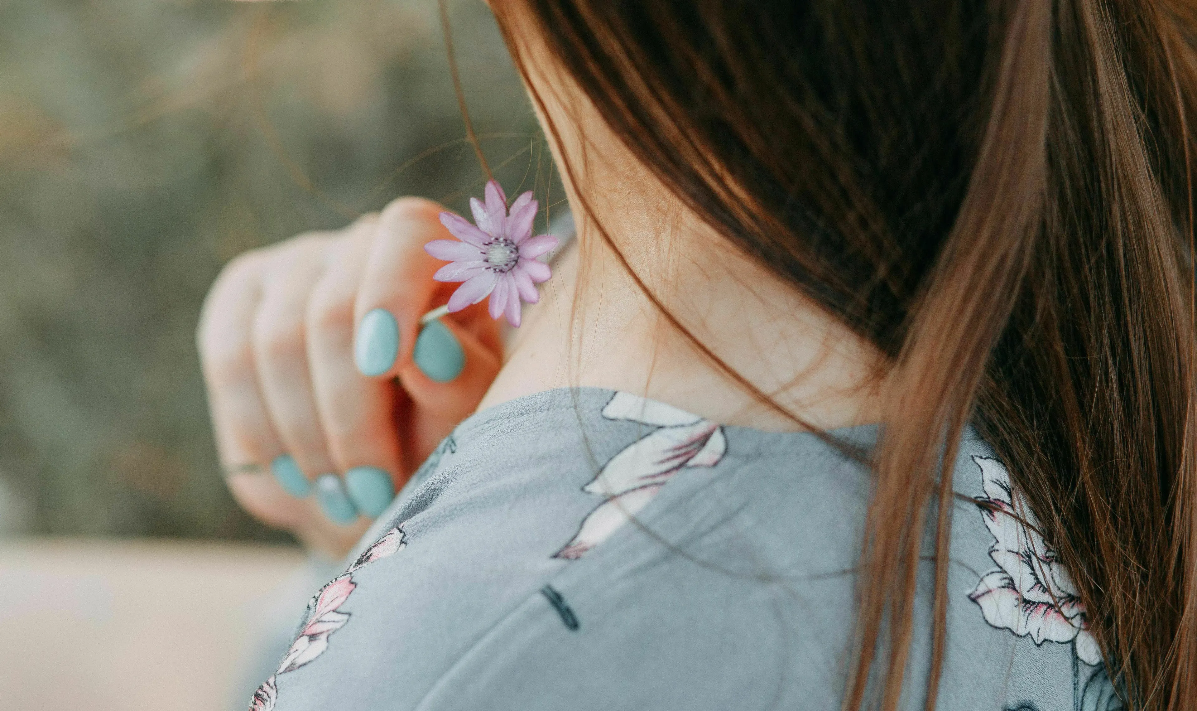 A woman holding a small purple flower by her neck. Her nails are painted light blue. Science Human Biology Trivia.