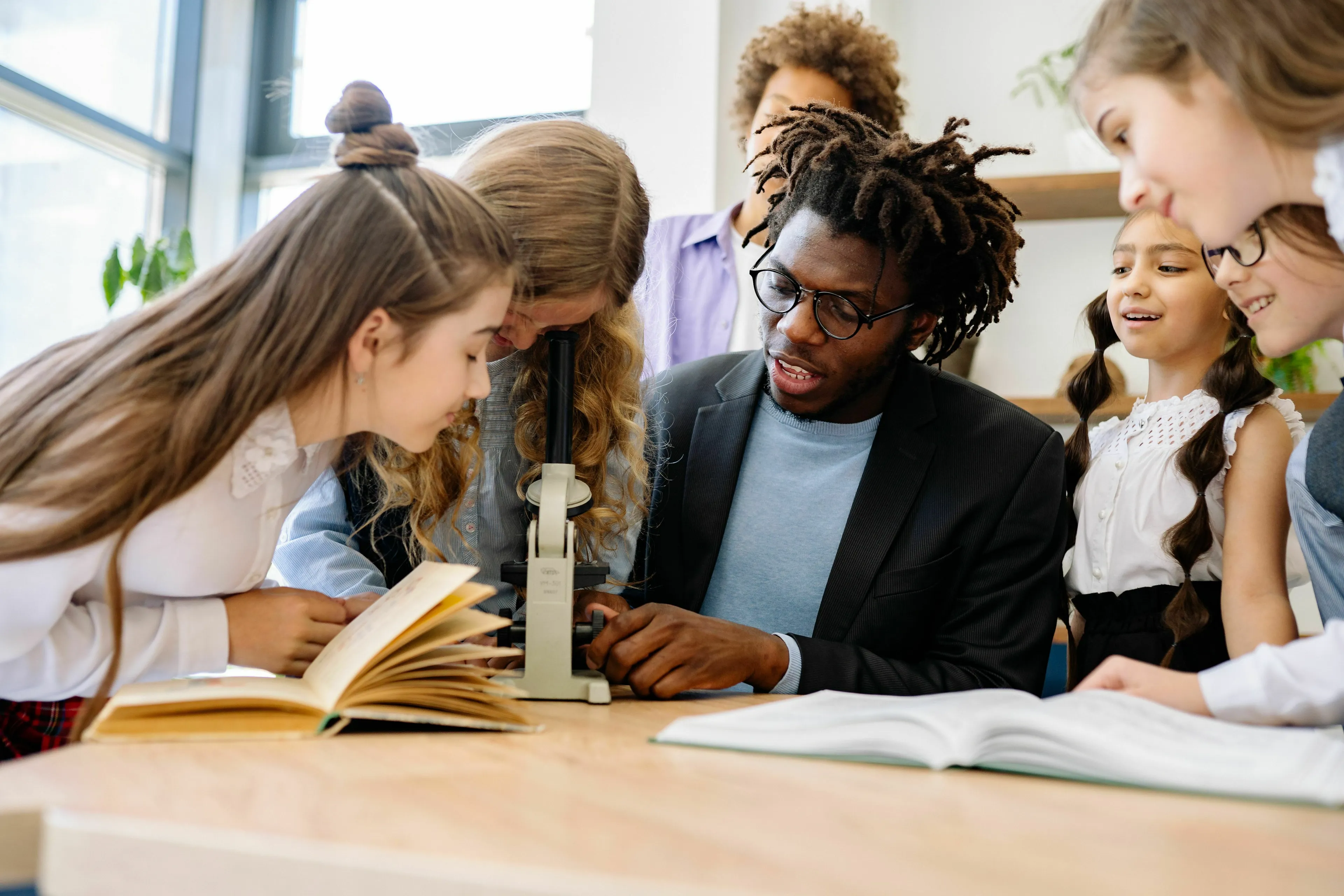 A male teacher helps young female students look into a microscope, exploring human biology and science trivia.