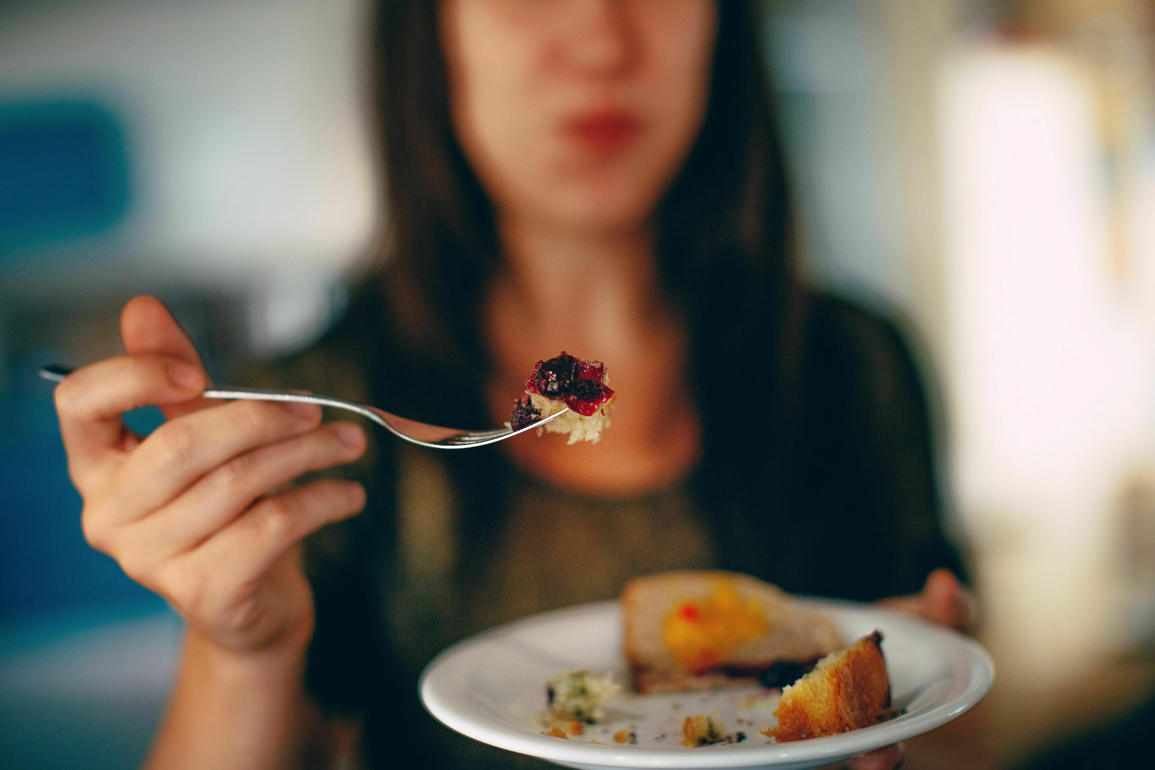 A person holding a fork with food and a plate with cake, illustrating the act of eating for human biology trivia.
