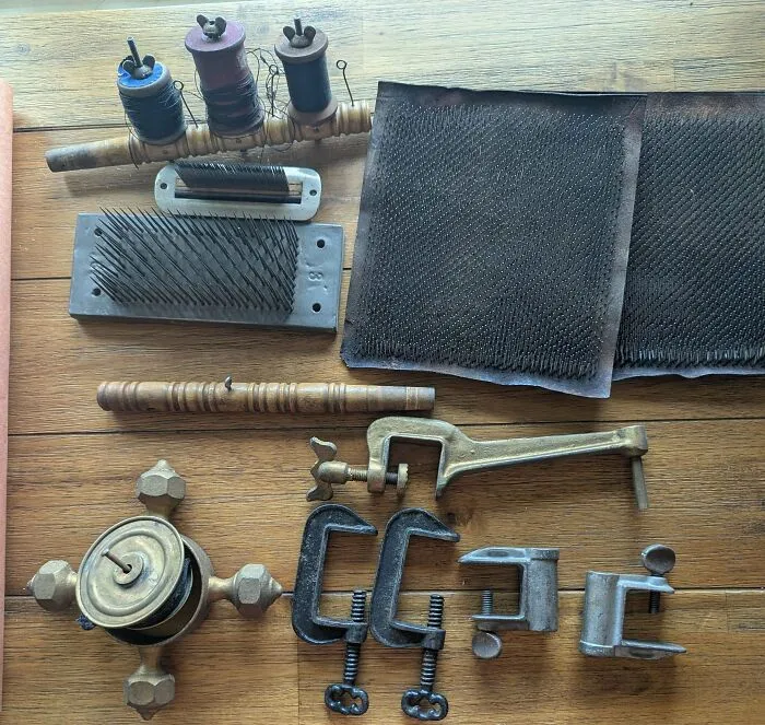 Assorted old treasures including spools, clamps, and carding tools laid out on a wooden surface