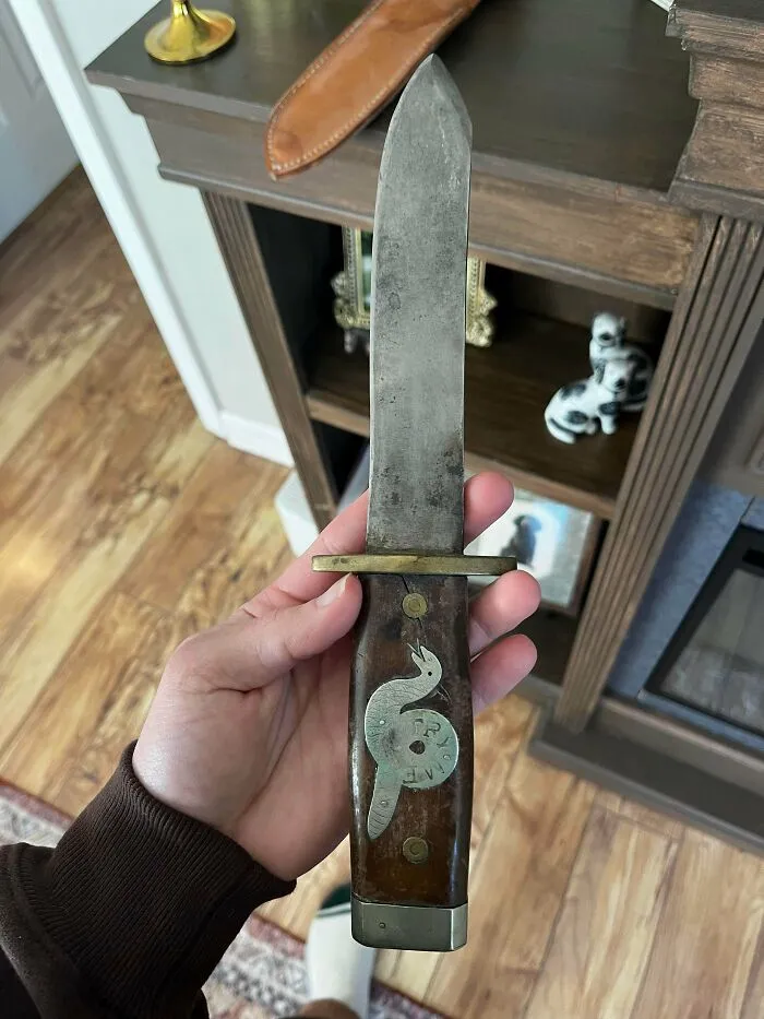 A hand holding a vintage knife with a decorated handle featuring a snake inlay, a unique old treasure discovery.