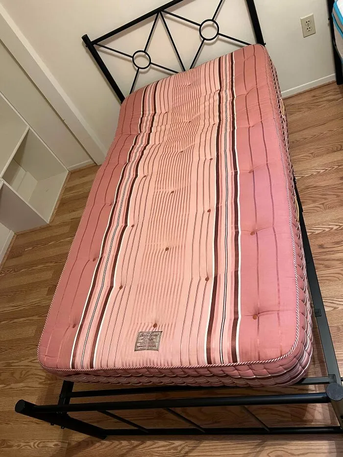 A vintage pink striped mattress resting on a metal bed frame, an interesting find among old treasures.